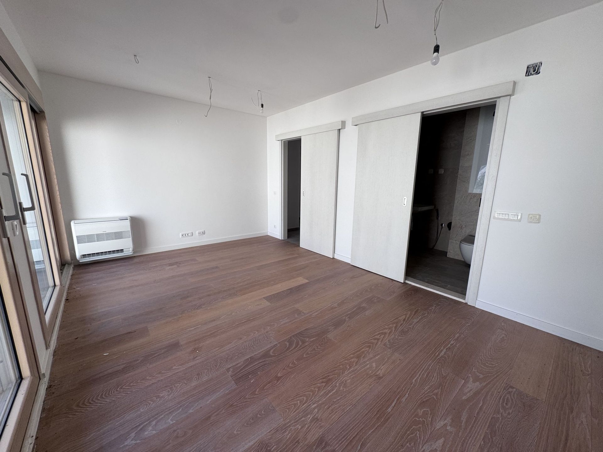 Svetla spavaća soba u novom stanu u Kotoru, Crna Gora: parketni pod, klizna vrata i izlaz na balkon.
