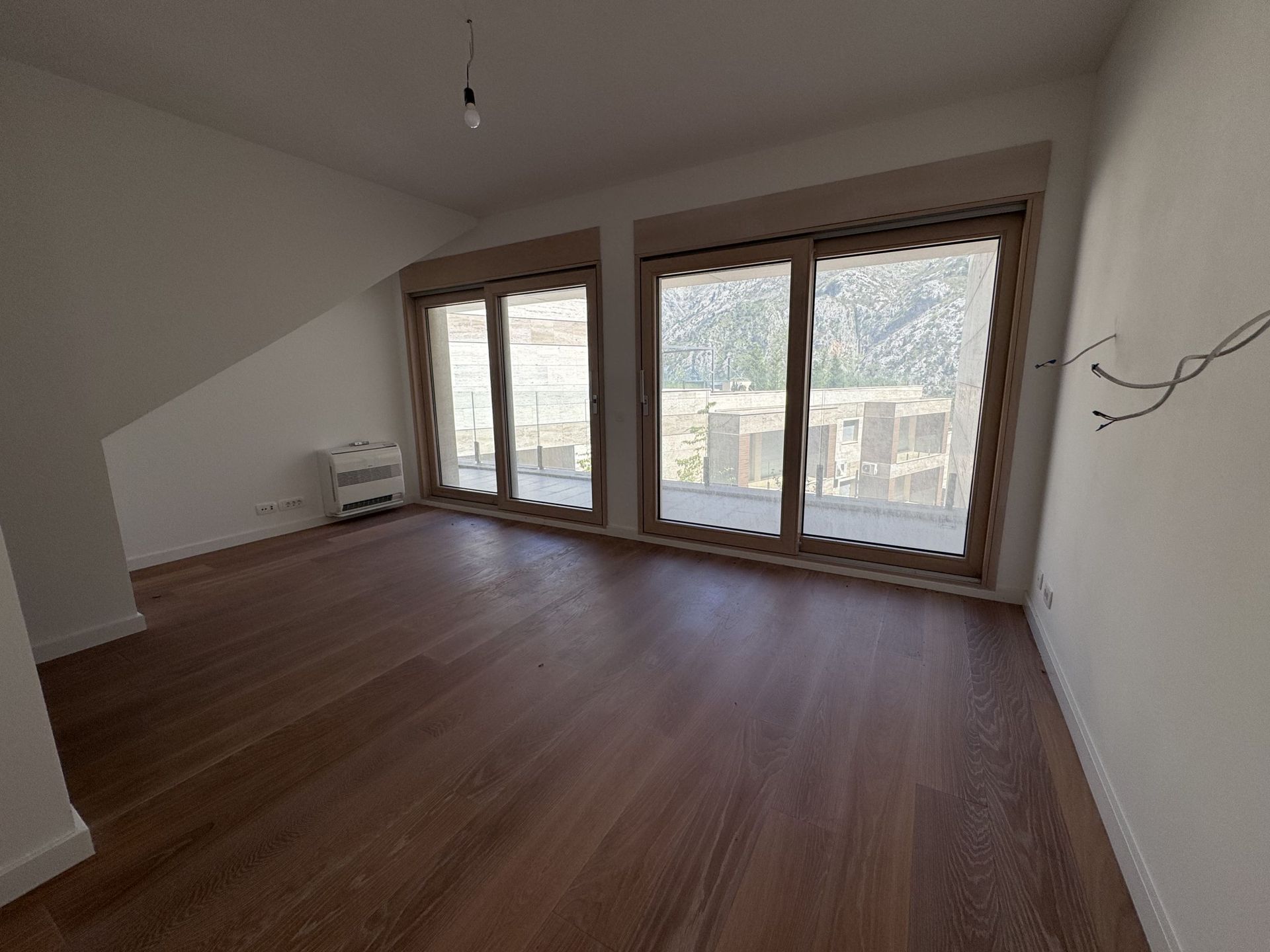 Svetao dnevni boravak u novogradnji u Kotoru, Crna Gora: panoramski prozori, pogled na planine, parket i izlaz na terasu.