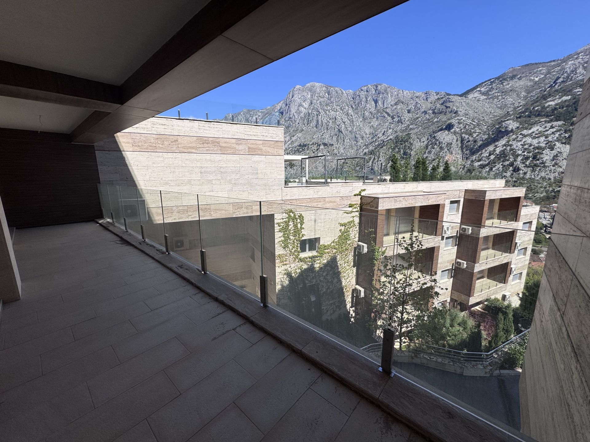 Prostrana terasa s panoramskim pogledom na planine u modernom stanu, Kotor, Crna Gora. Završna obrada kamenom i staklom.