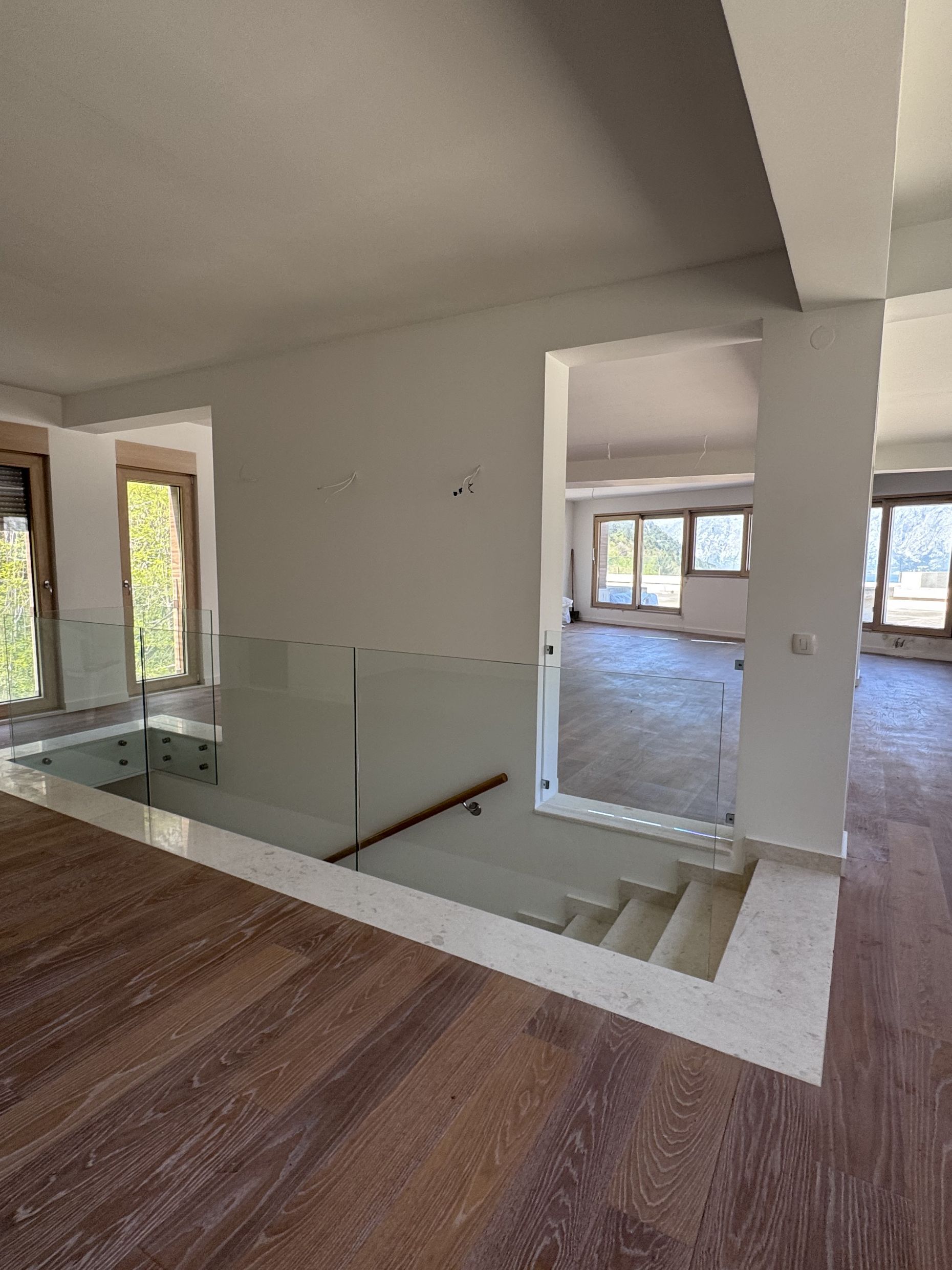 Enterijer dnevne sobe sa stepeništem i staklenom ogradom u novom stanu u Kotoru, Crna Gora. Svetla završna obrada.