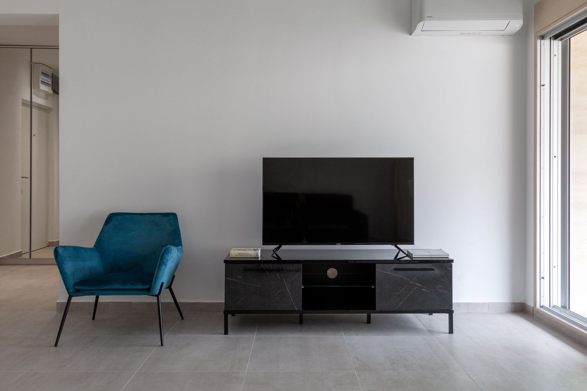 Modernes Wohnzimmer in einer Wohnung in Kotor, Montenegro: blauer Sessel, TV-Möbel in Marmoroptik und Panoramaverglasung.