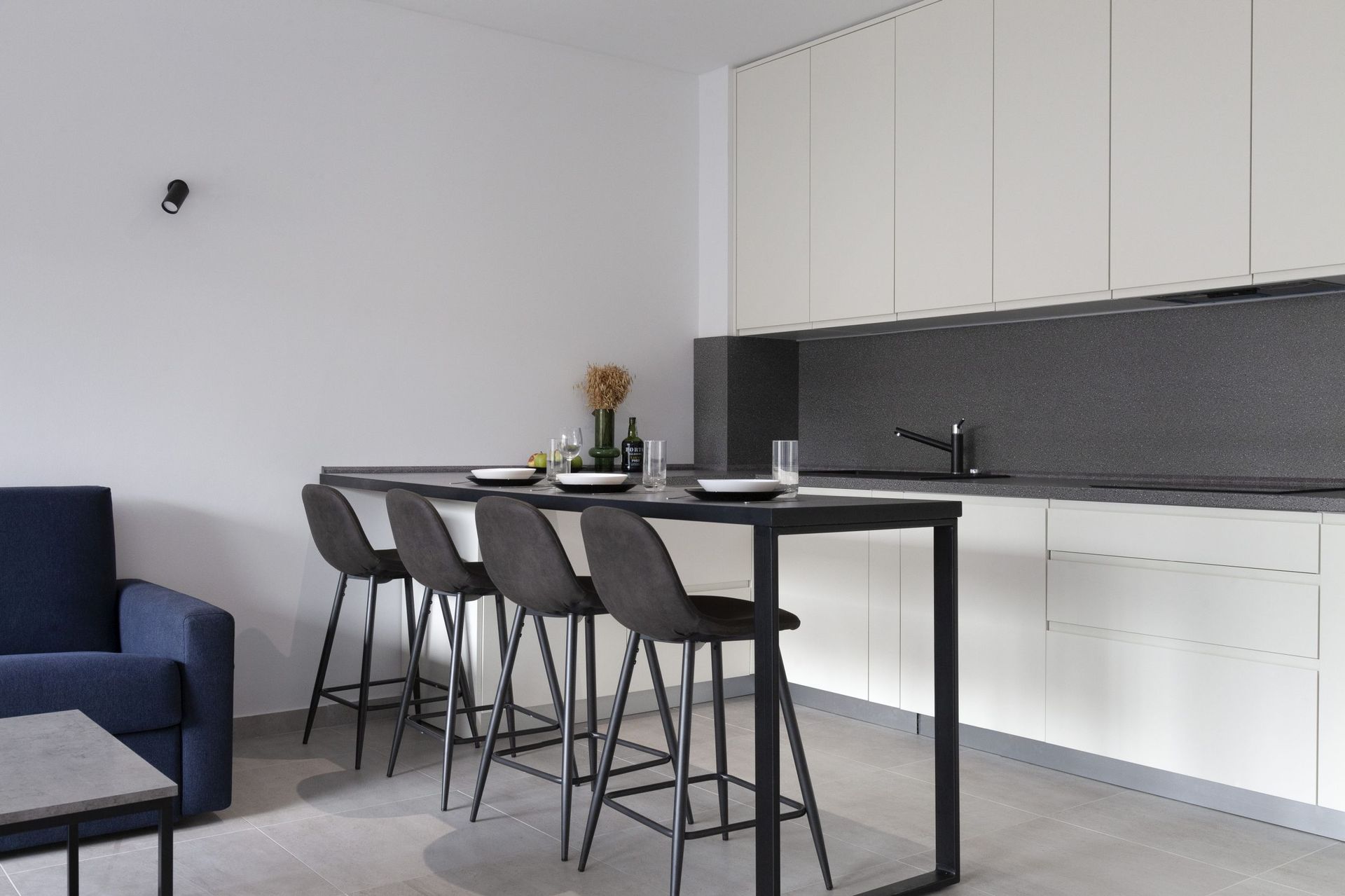 Moderne Küche in einer Wohnung in Kotor, Montenegro: weiße Fronten, dunkle Arbeitsplatte und Bartheke mit hohen Stühlen.