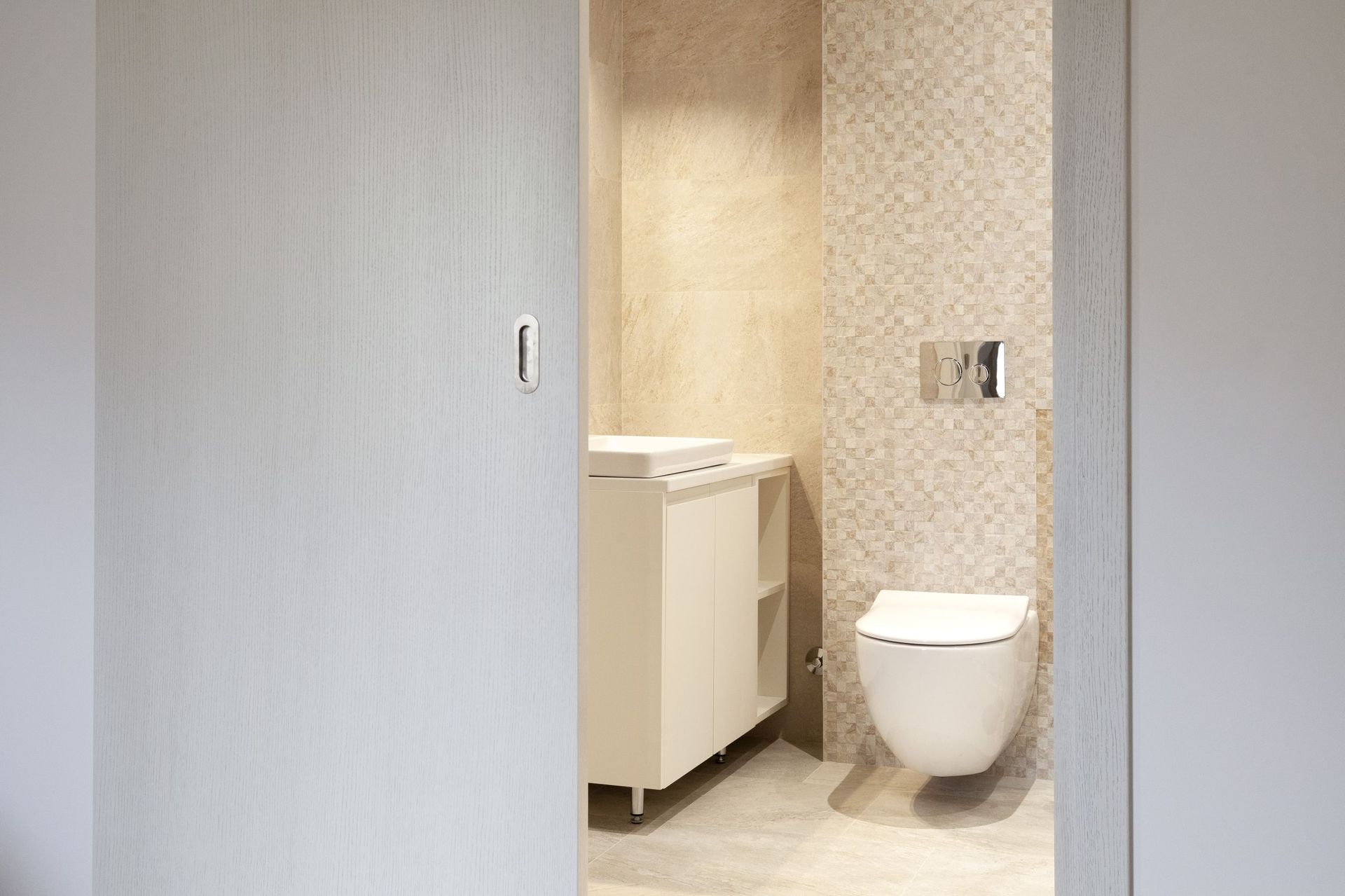 Modernes Badezimmer in einer Wohnung in Kotor, Montenegro: Hänge-WC, Waschtisch und beige Fliesen.