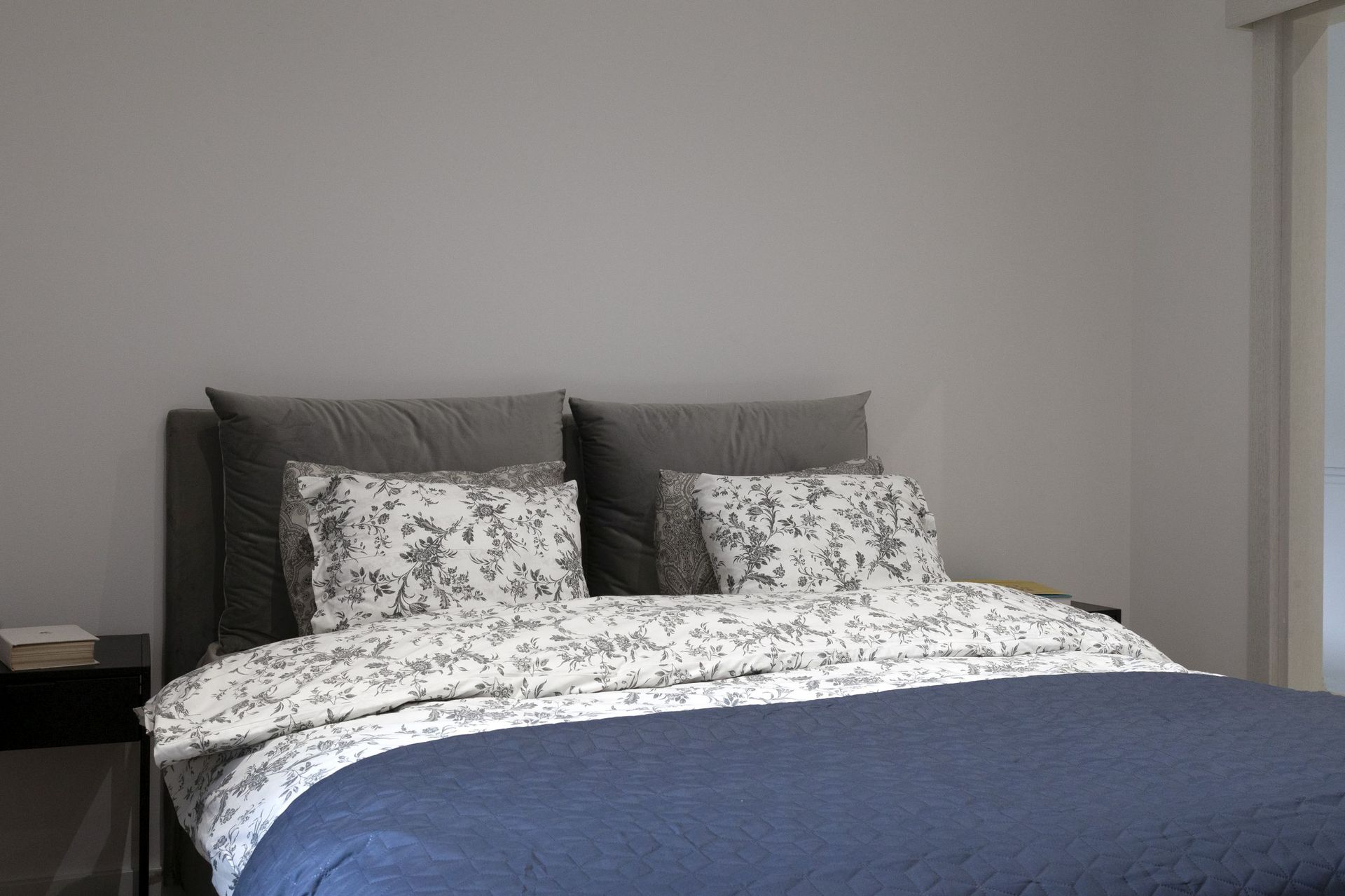 Modernes Schlafzimmer in einer Wohnung in Kotor, Montenegro: Doppelbett mit grauem Kopfteil und blauer Tagesdecke.