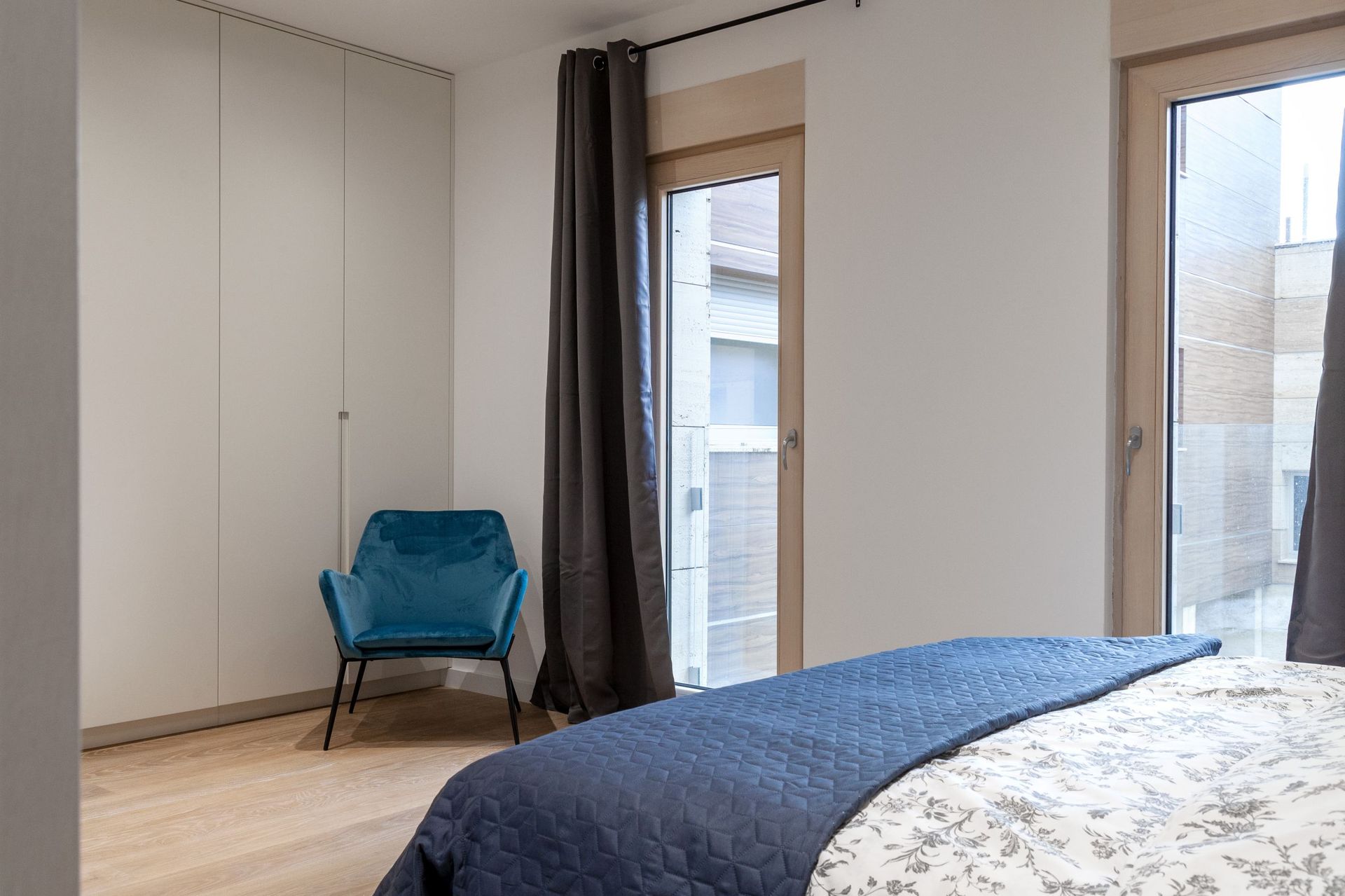 Modernes Schlafzimmer in einer Wohnung in Kotor, Montenegro: blauer Sessel, Einbauschrank und Zugang zur Terrasse.