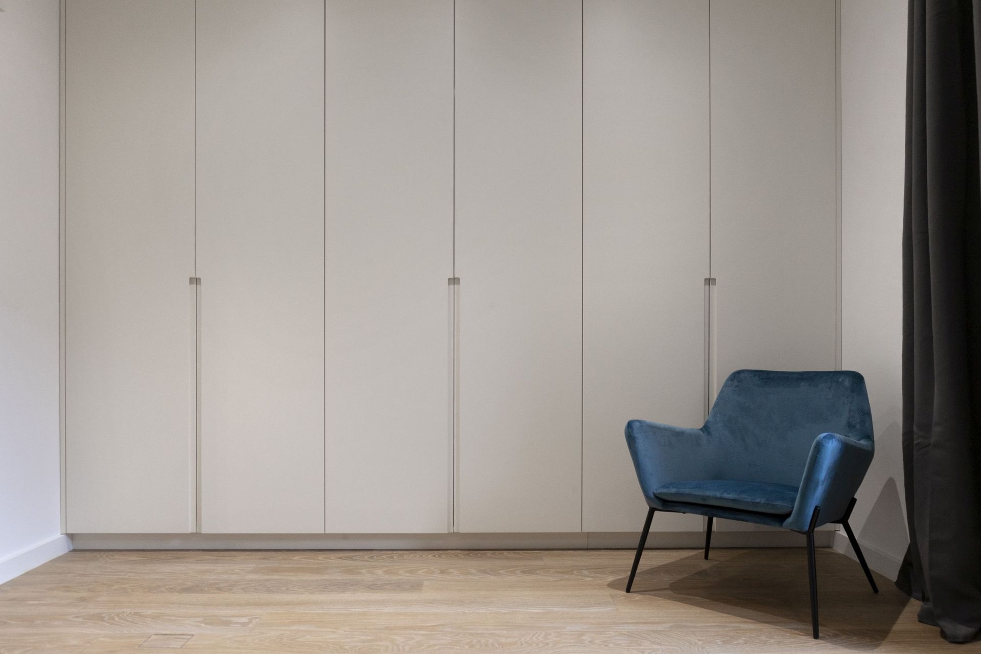 Modernes Schlafzimmer in einer Wohnung in Kotor, Montenegro: eingebauter weißer Schrank, blauer Samtsessel und Parkettboden.
