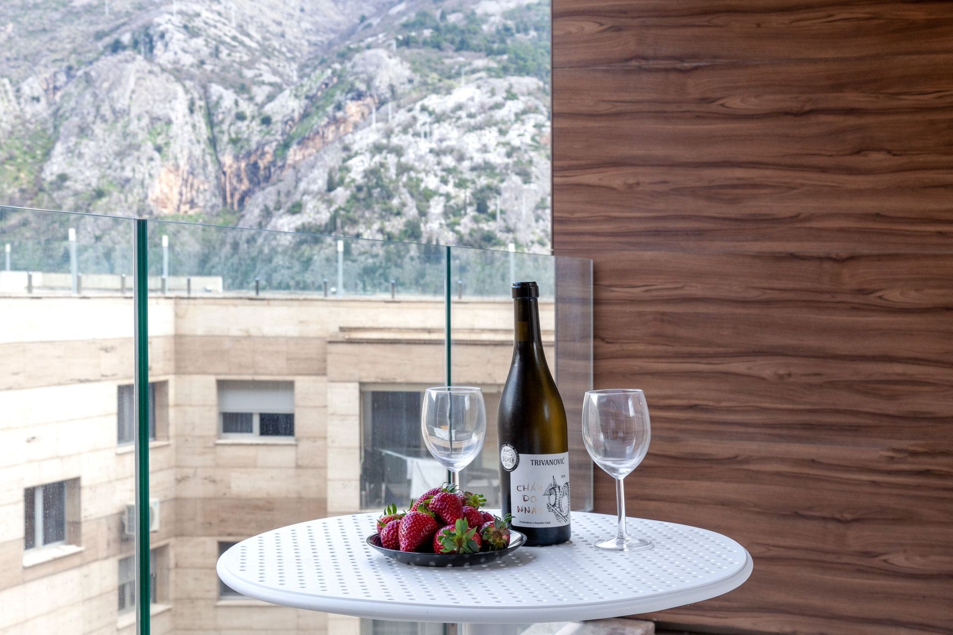 Balkon der Wohnung in Kotor, Montenegro: Tisch mit Wein und Erdbeeren vor Bergpanorama und moderner Ausstattung.