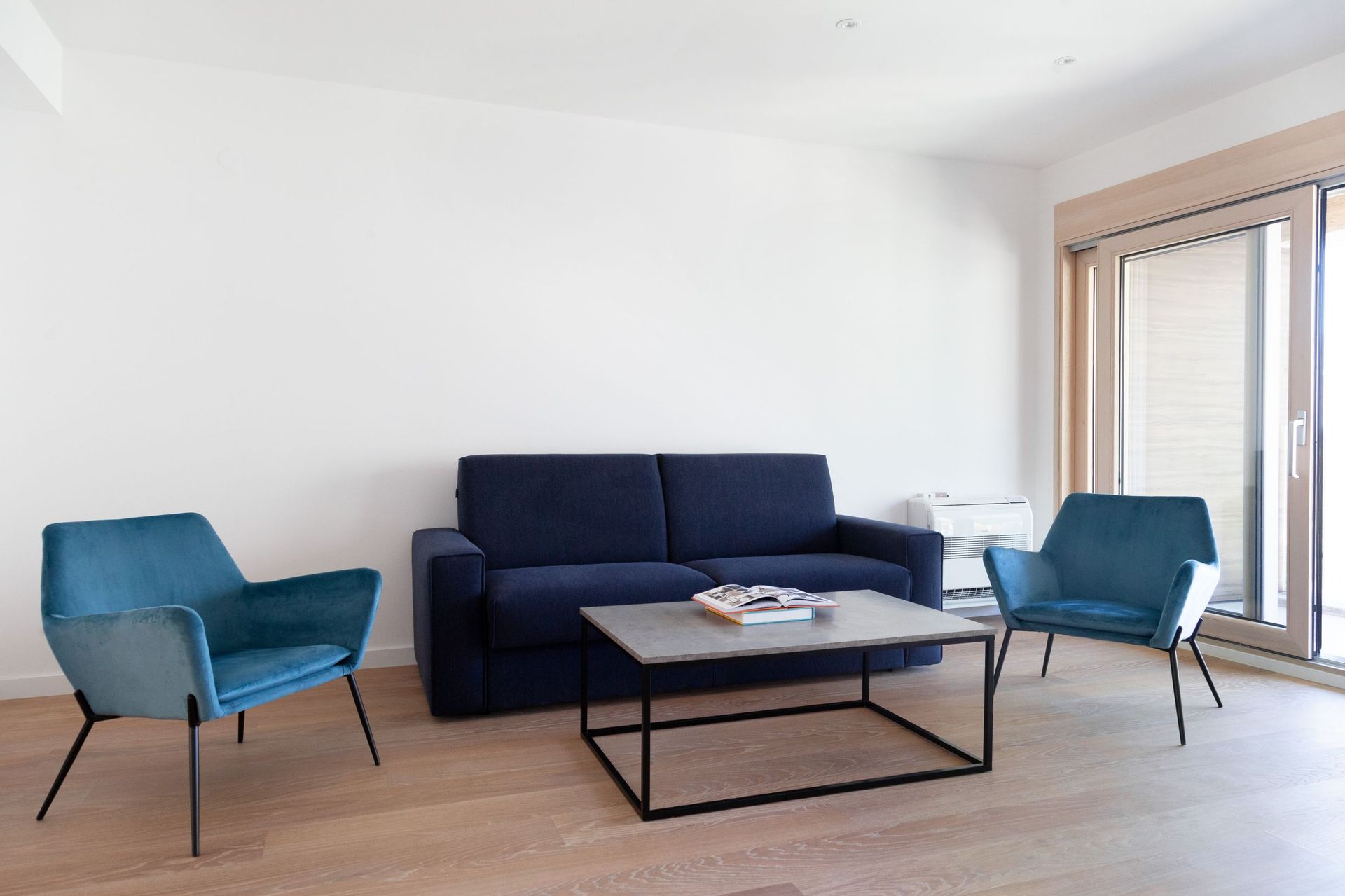 Wohnzimmer in einer Wohnung in Kotor, Montenegro: blaues Sofa, zwei Sessel, Couchtisch und Panoramafenster mit Ausgang.