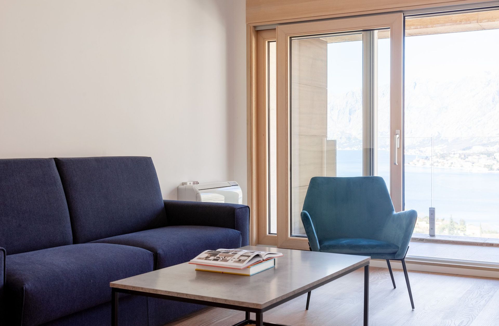 Wohnzimmer mit blauem Sofa und Sessel in einer Wohnung in Kotor, Montenegro, mit Panoramablick auf Meer und Berge durch den Balkon.