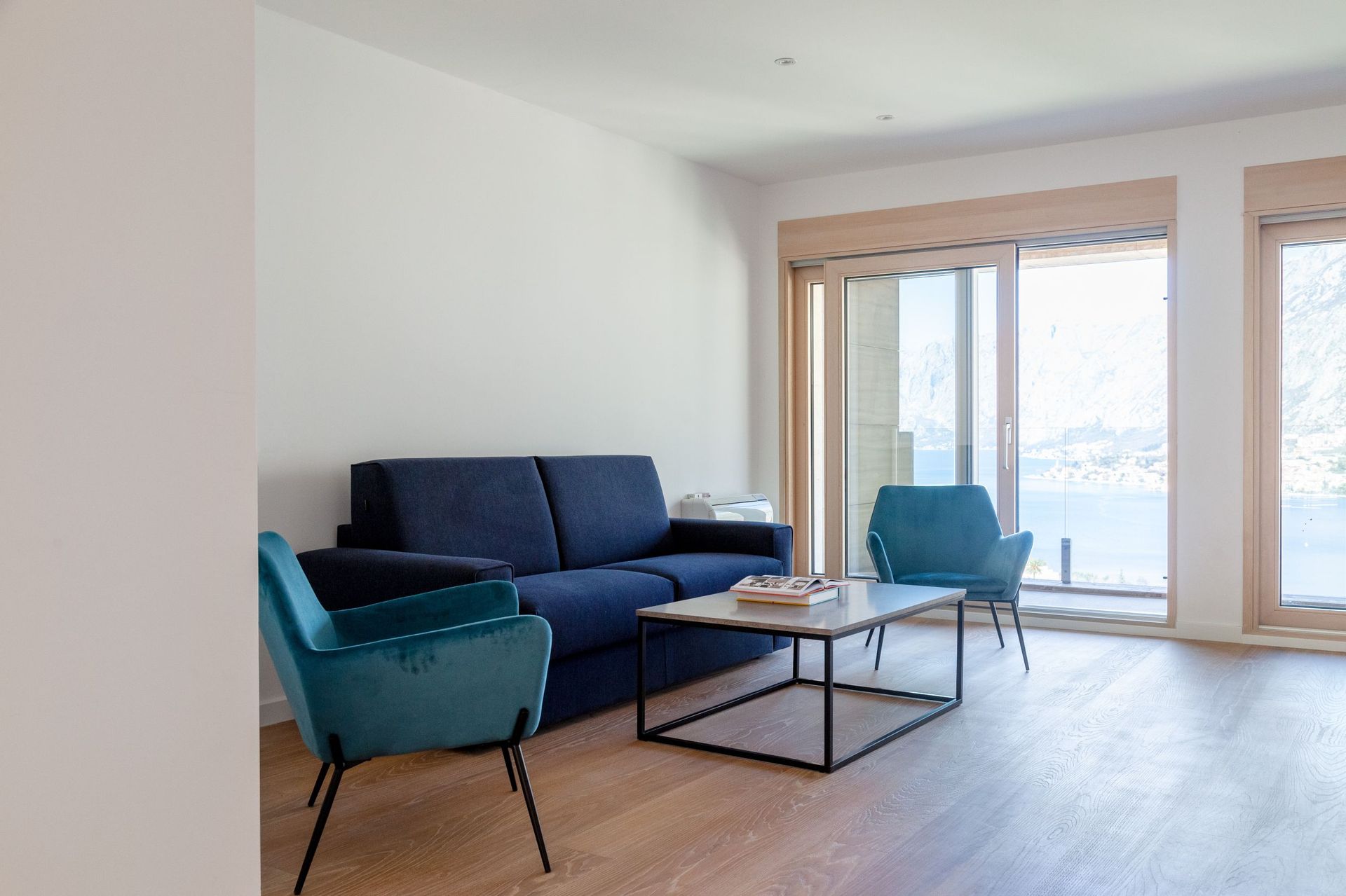 Modernes Wohnzimmer in einer Wohnung in Kotor, Montenegro: blaues Sofa, Sessel, Panoramablick auf die Bucht von Kotor und die Berge.