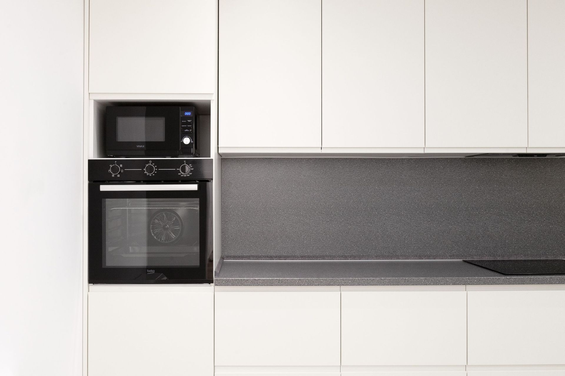 Moderne weiße Küche mit grauer Arbeitsplatte und eingebauten Beko-Geräten in einer Wohnung in Kotor, Montenegro.