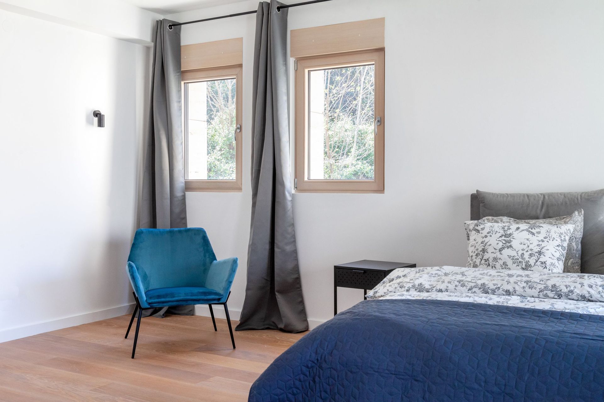 Modernes Schlafzimmer in einer Wohnung in Kotor, Montenegro: blauer Sessel, Doppelbett, heller Parkettboden und Blick auf den Garten.