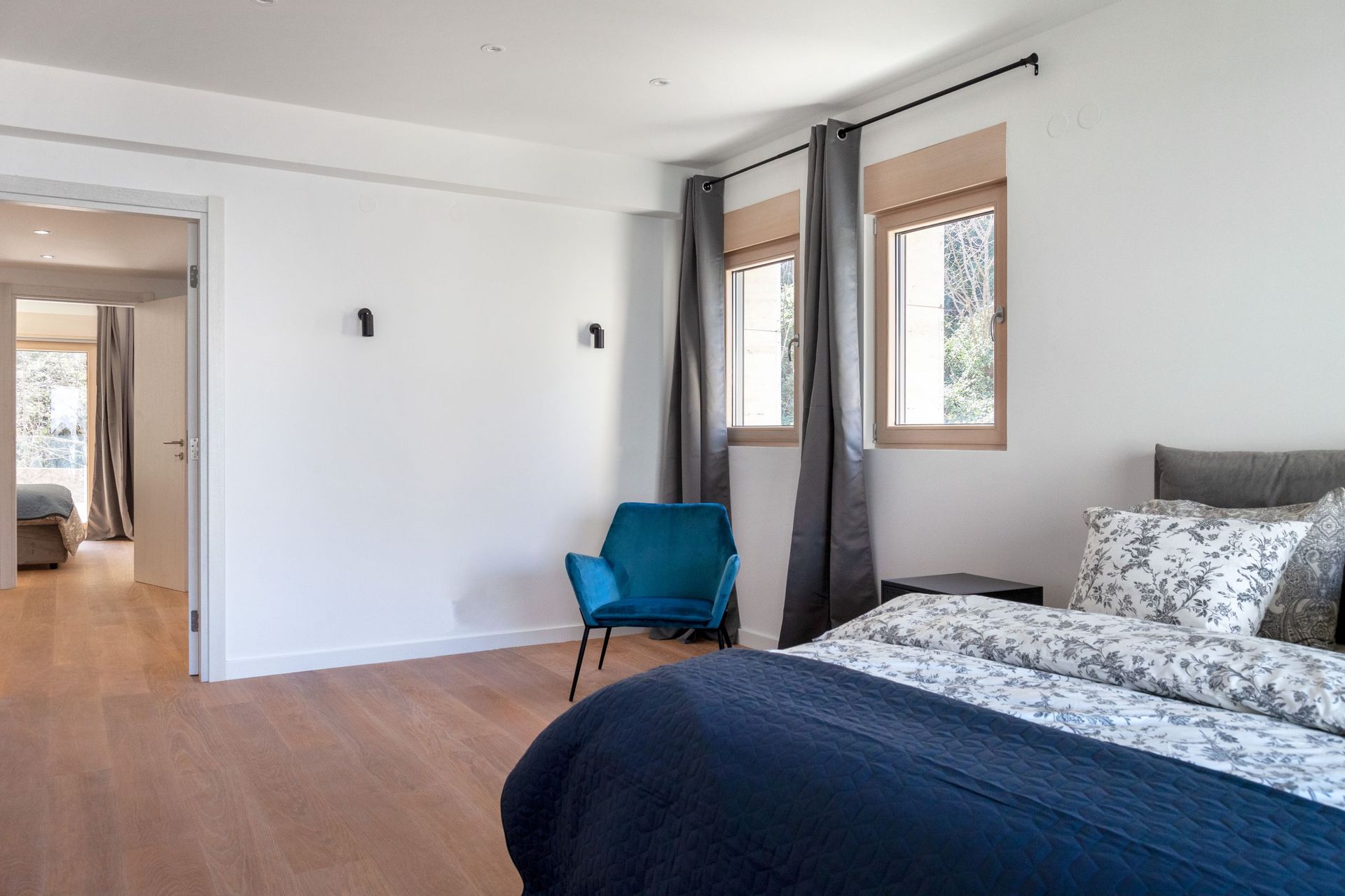 Modernes Schlafzimmer in einer Wohnung in Kotor, Montenegro: blauer Sessel, Doppelbett, heller Parkettboden und Blick aus dem Fenster.