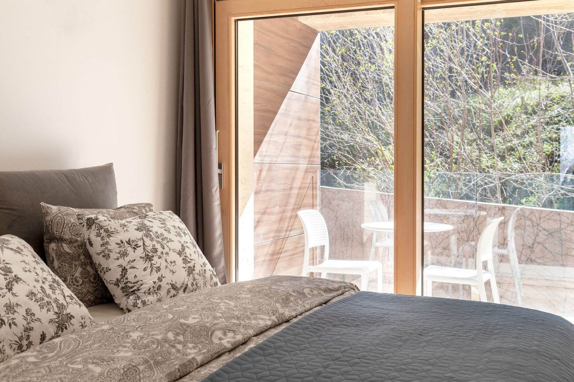 Schlafzimmer in einer Wohnung in Kotor, Montenegro: Doppelbett, Panoramafenster und Zugang zur Terrasse mit Gartenmöbeln.