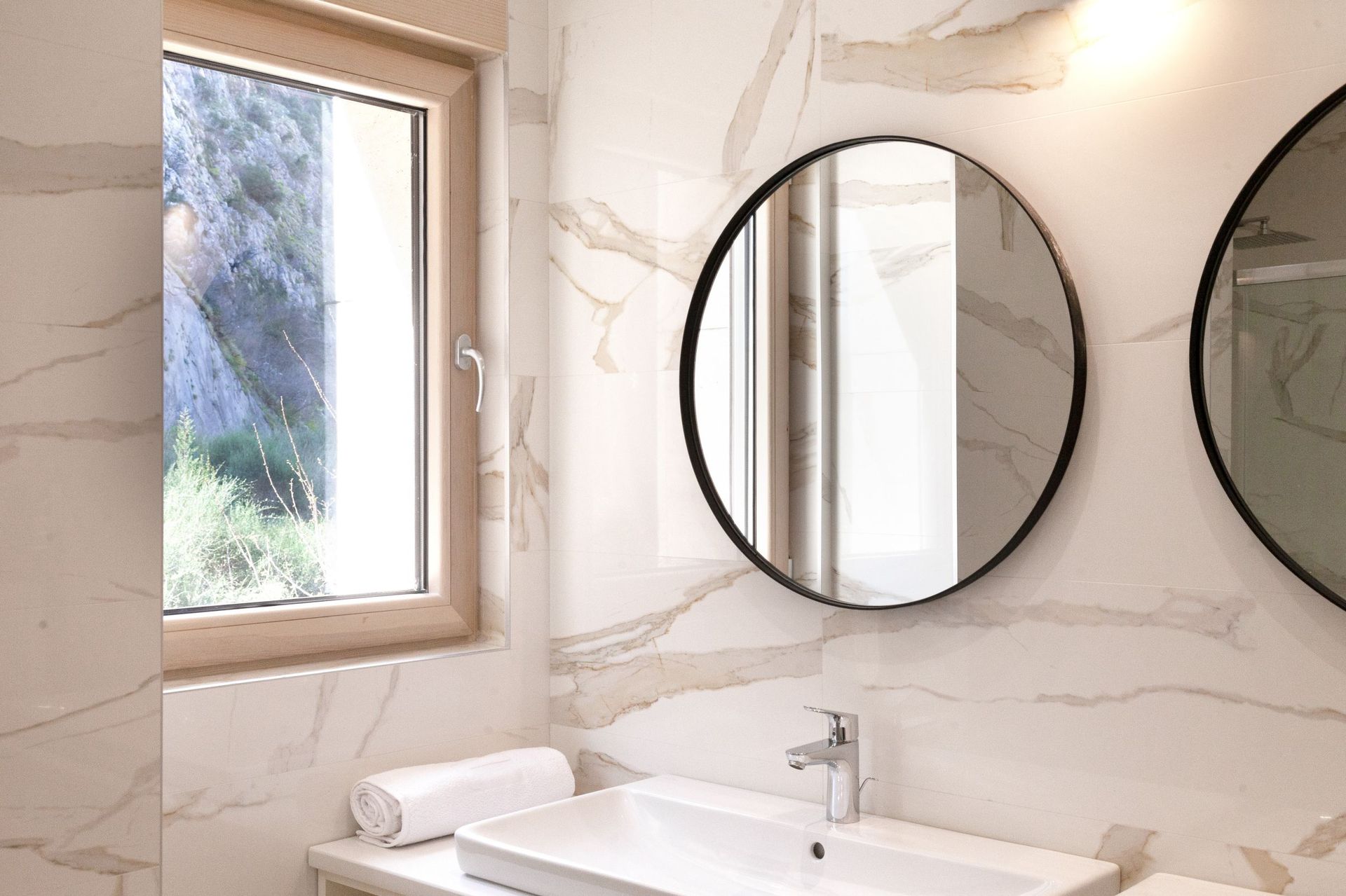 Modernes Badezimmer mit Marmoroptik in einer Wohnung in Kotor, Montenegro, mit rundem Spiegel und Bergblick.