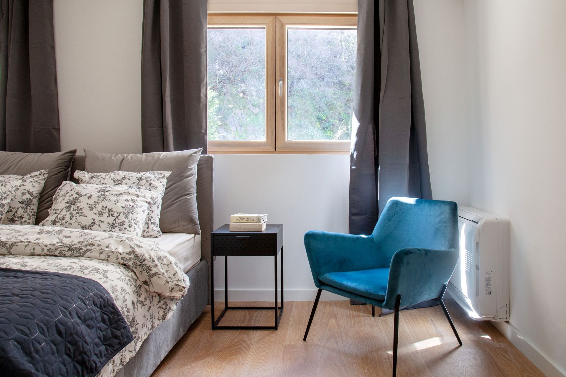 Modernes Schlafzimmer in einer Wohnung in Kotor, Montenegro: Doppelbett, blauer Sessel und Bergblick aus dem Fenster.