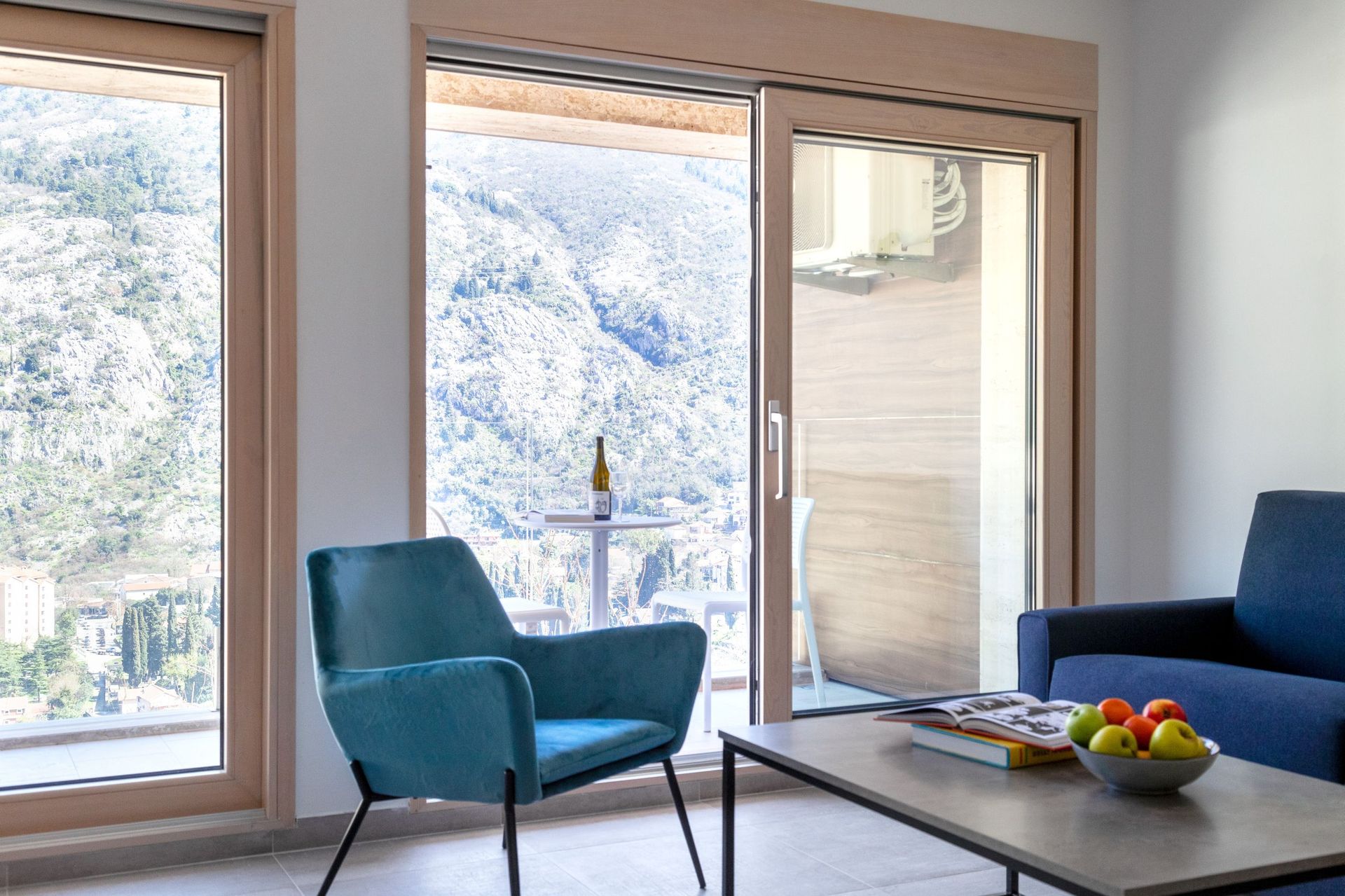 Wohnzimmer mit Panoramablick auf die Berge und Kotor in Montenegro, moderne Möbel und Zugang zur Terrasse.