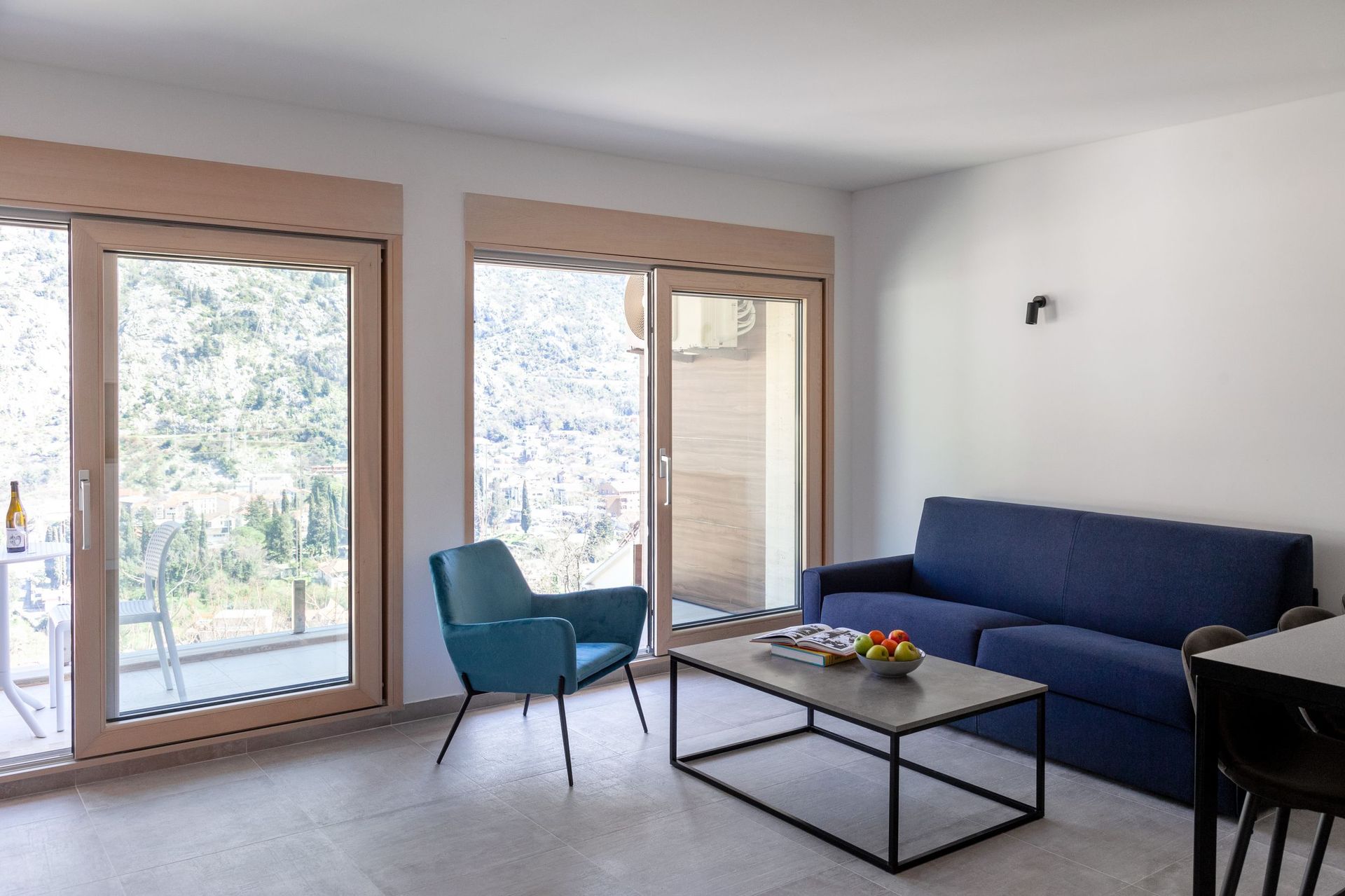 Modernes Wohnzimmer in einer Wohnung in Kotor, Montenegro: blaues Sofa, Sessel, Panoramafenster mit Bergblick.
