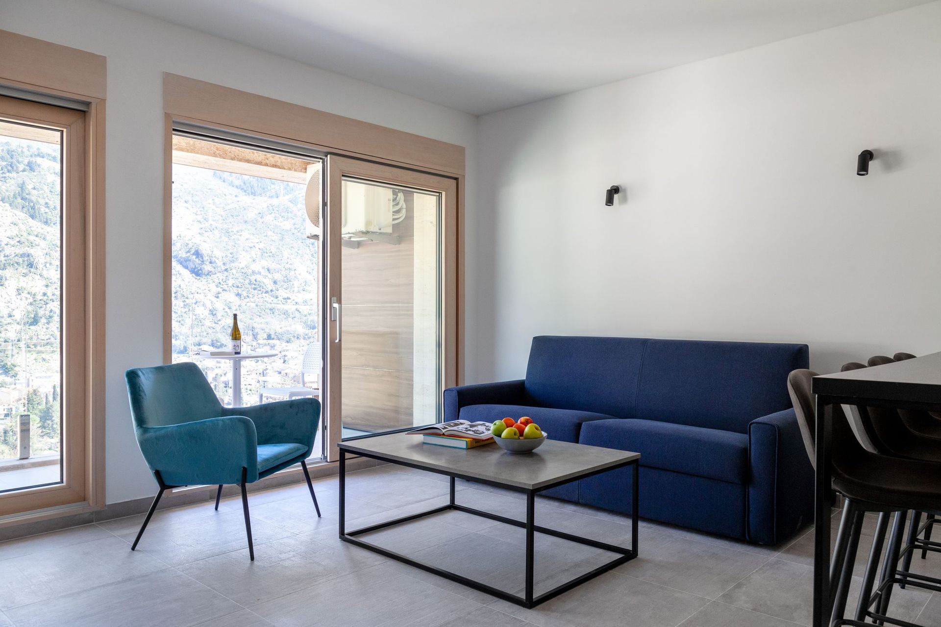 Wohnzimmer in einer Wohnung in Kotor, Montenegro: blaues Sofa, Sessel, Panoramafenster mit Bergblick und Terrasse.