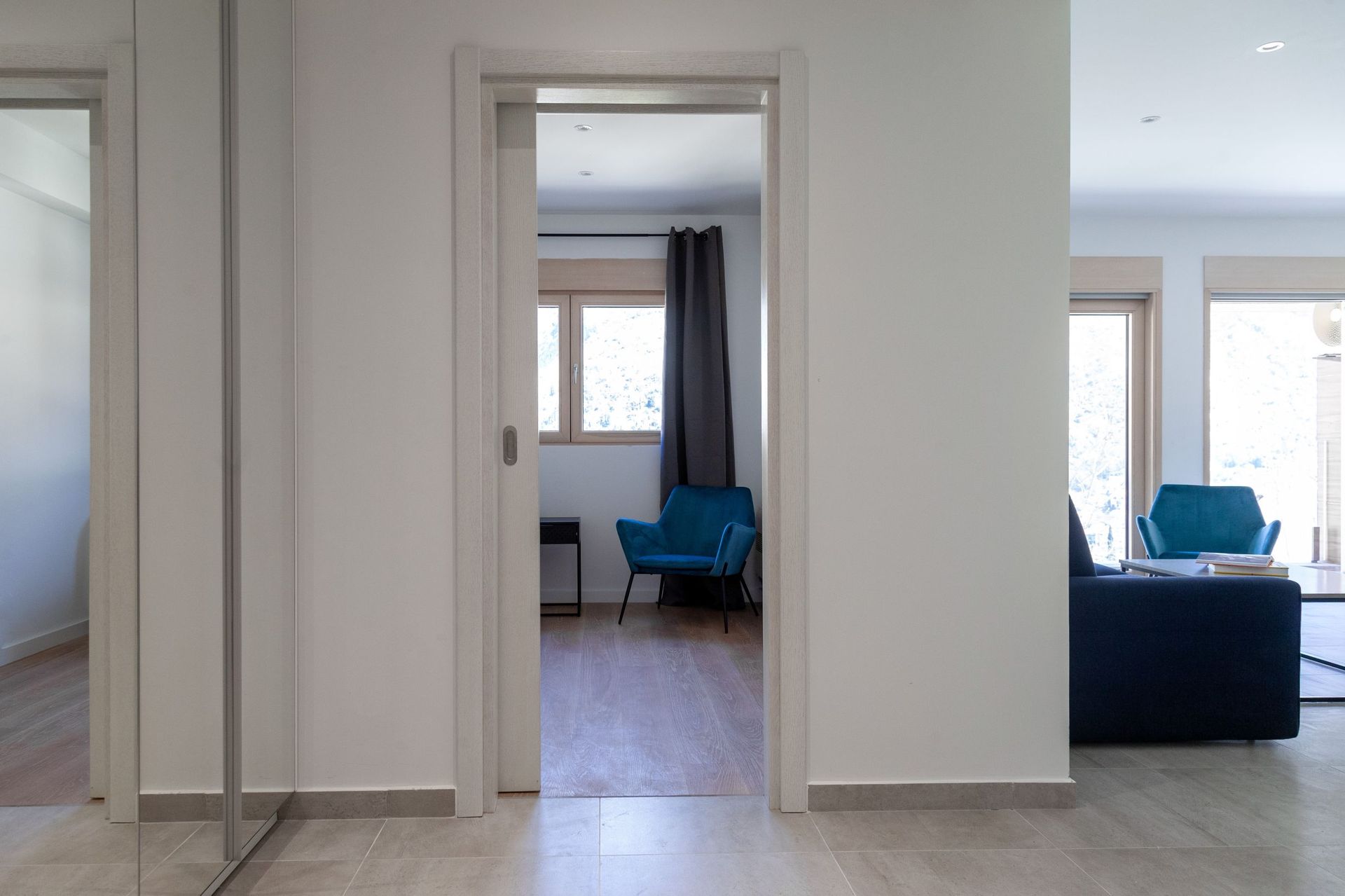 Innenraum einer modernen Wohnung in Kotor, Montenegro: helles Wohnzimmer mit blauen Sesseln, Holzboden und Aussicht.