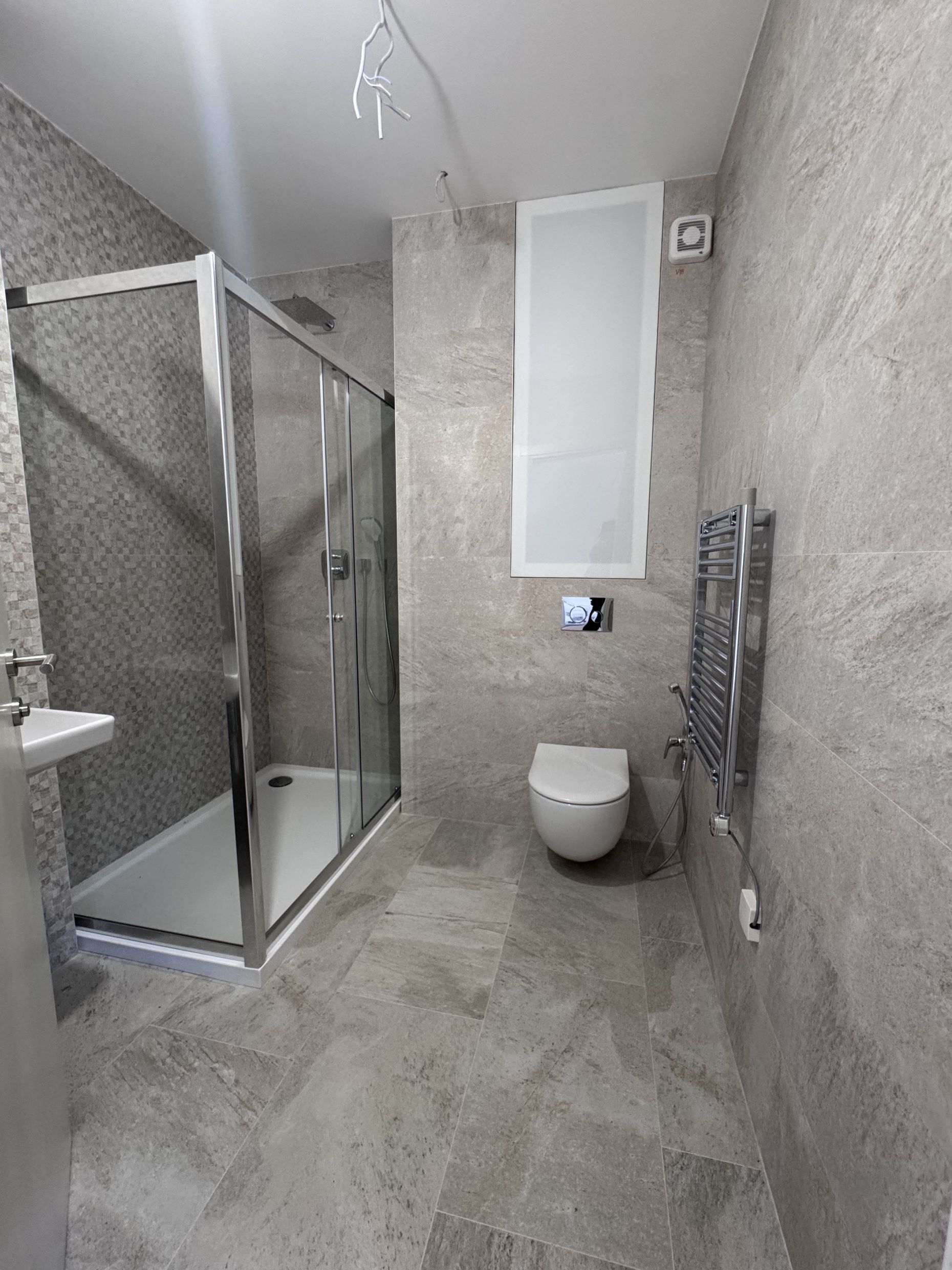 Modern bathroom in a duplex, Kotor, Montenegro: shower cabin, wall-hung toilet, and stone-look tiles.