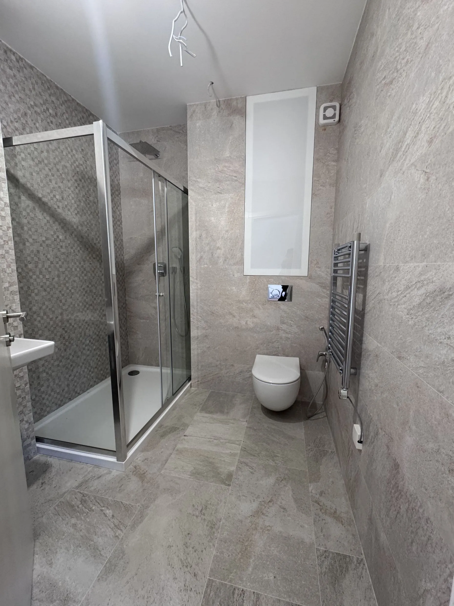 Moderne Baderum mit Glasduschkabine, wandmontierter Toilette und grauen Steinoptik-Fliesen.