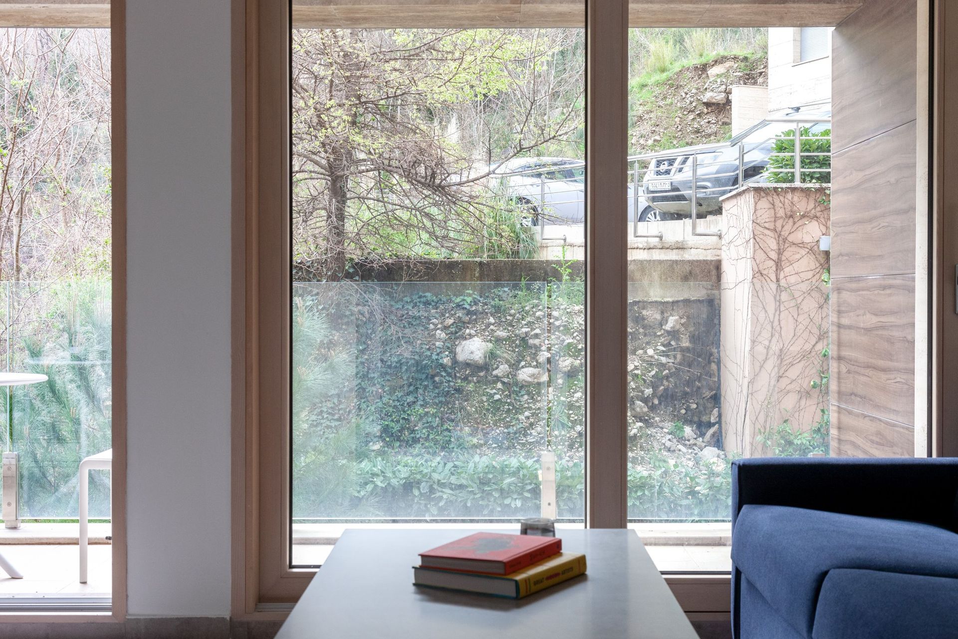 Blick vom Wohnzimmer auf die Terrasse und den Garten in einer Wohnung in Kotor, Montenegro: Panoramafenster, blauer Sessel und Couchtisch.