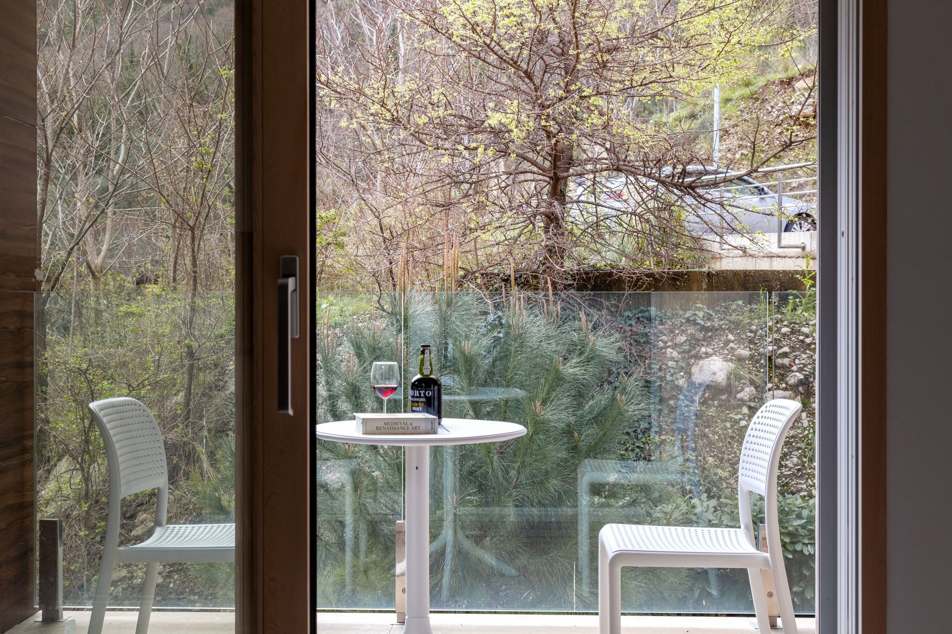 Balkon einer Wohnung in Kotor, Montenegro: Tisch mit Wein und Blick auf den grünen Garten durch die Glasbrüstung.