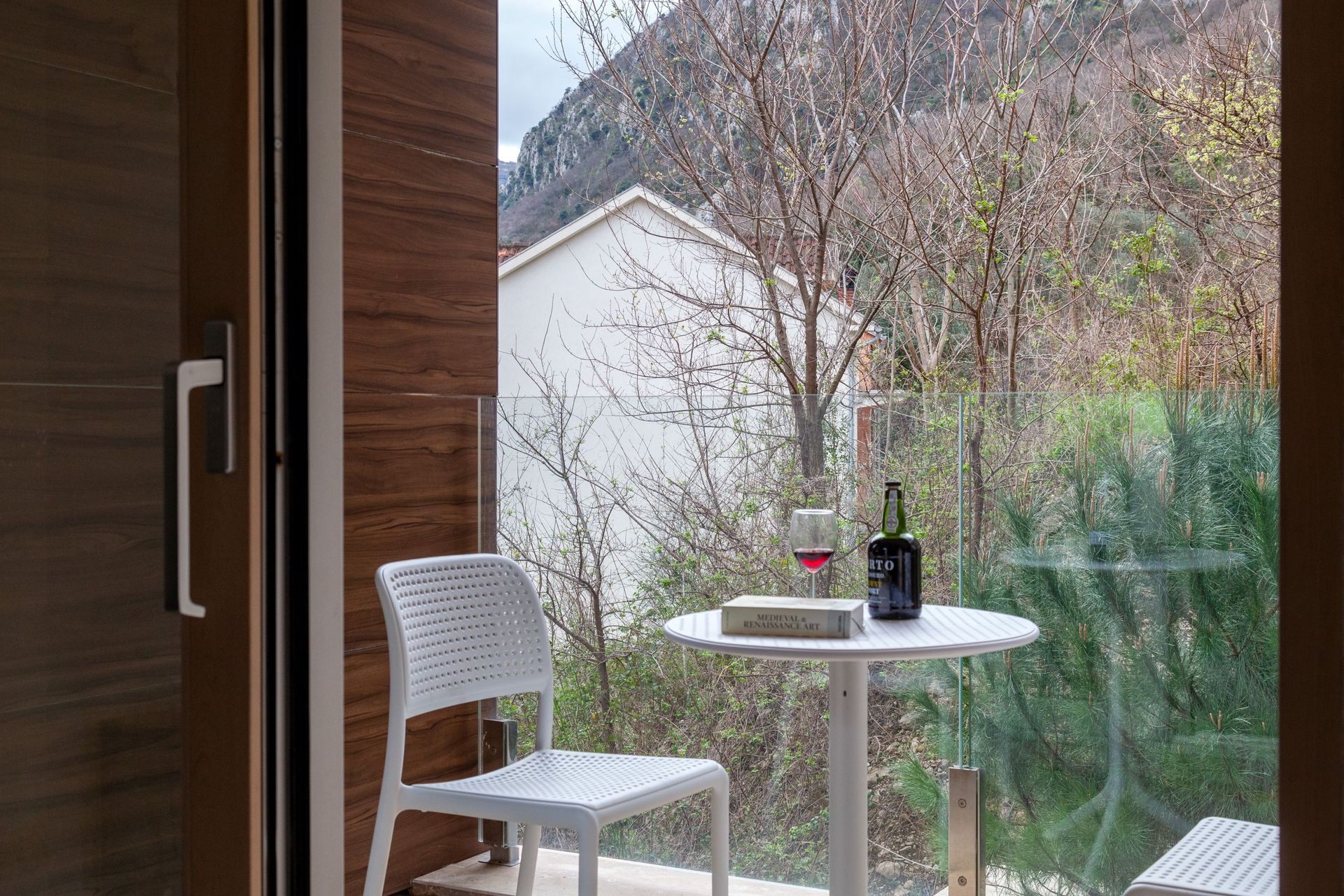 Balkon mit weißen Möbeln und Bergblick in einer Wohnung, Kotor, Montenegro. Gemütliche Sitzecke mit Panoramaverglasung.