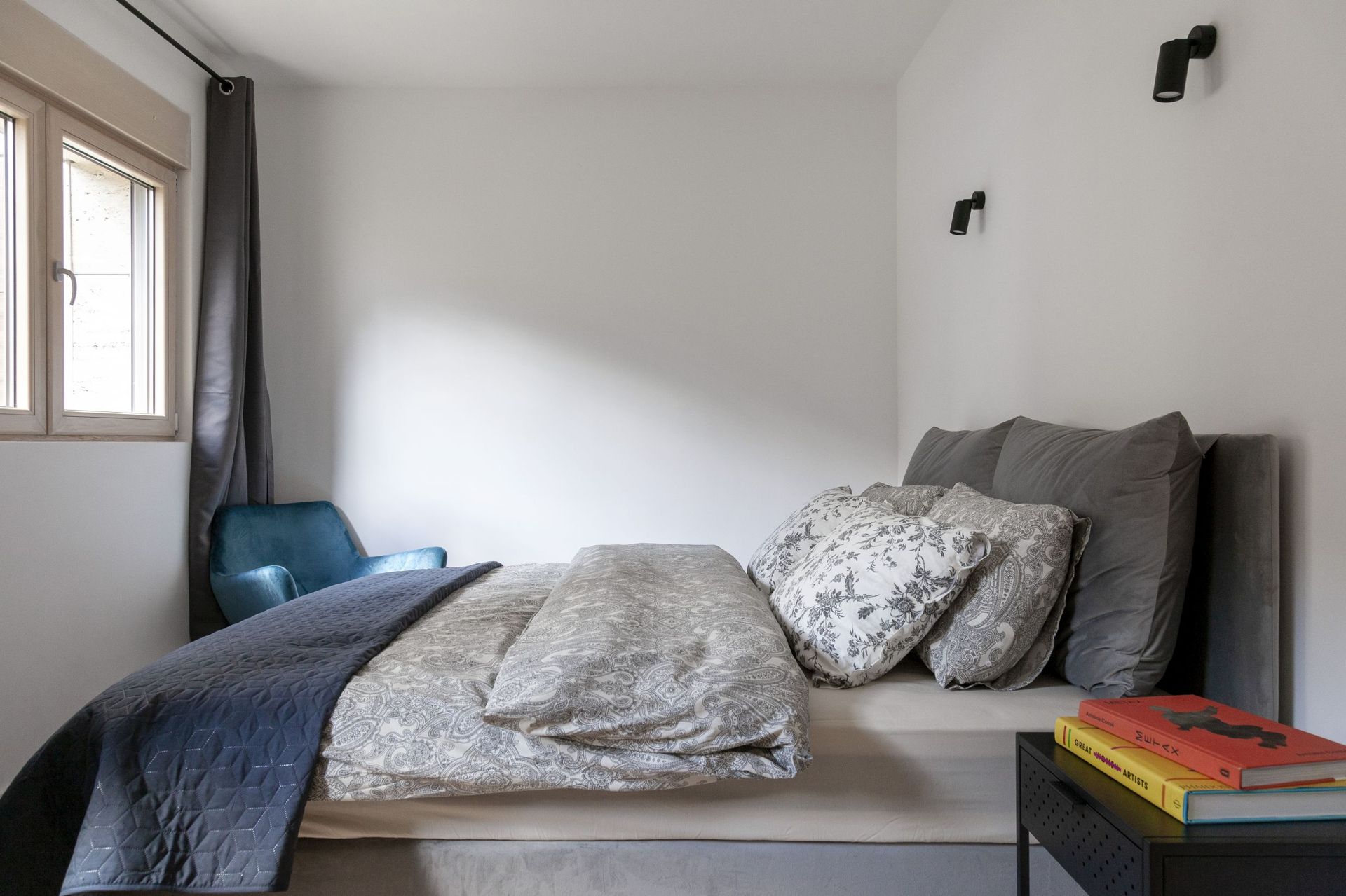 Modernes Schlafzimmer in einer Wohnung in Kotor, Montenegro: Doppelbett, blauer Sessel und stilvolle Beleuchtung.