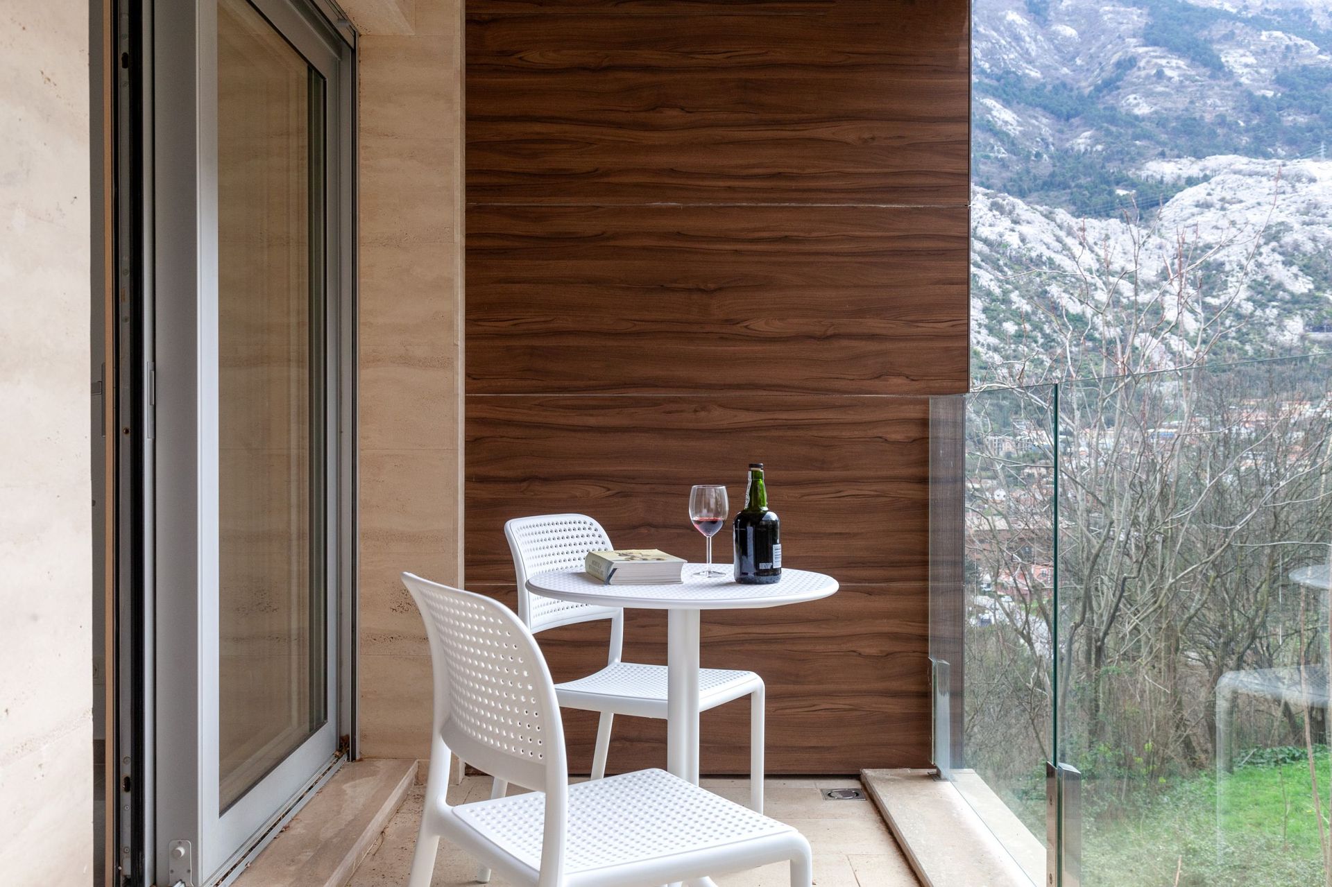 Balkon der Wohnung in Kotor, Montenegro: weiße Möbel, Holzoptik, Glasgeländer und Bergblick.