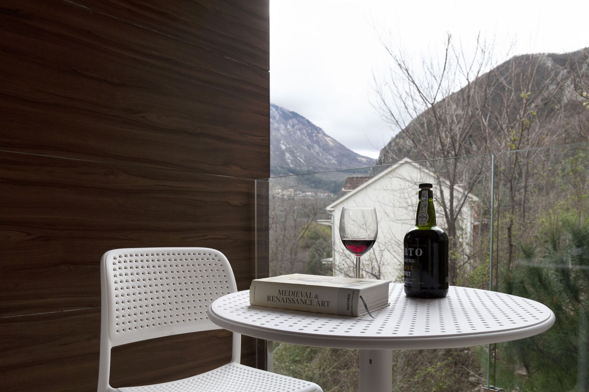 Balkon der Wohnung in Kotor, Montenegro: weißer Tisch, Stuhl, Blick auf die Berge und Wandverkleidung in Holzoptik.