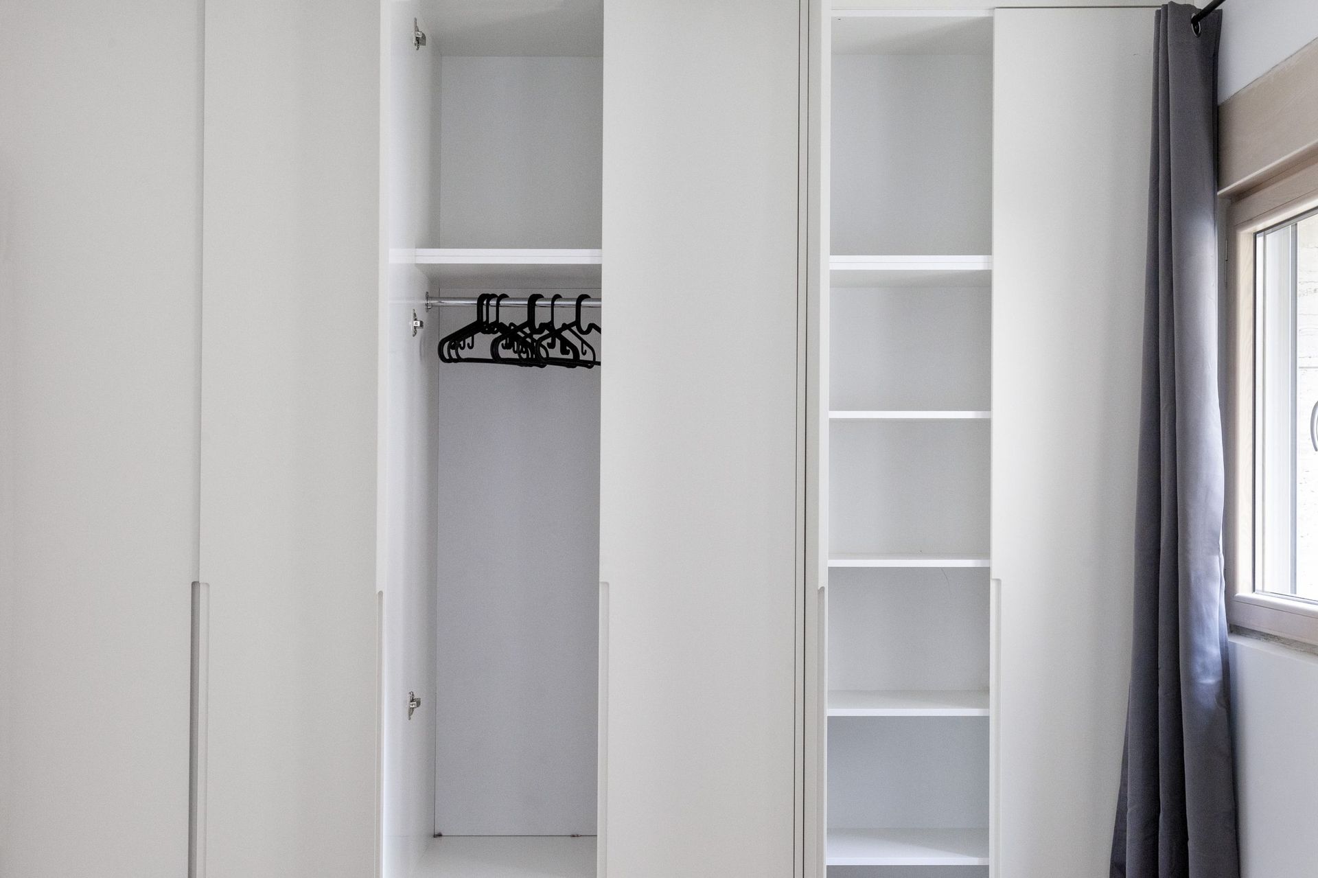 Einbauschrank in Weiß mit Regalen und Kleiderstangen im Schlafzimmer der Wohnung in Kotor, Montenegro.