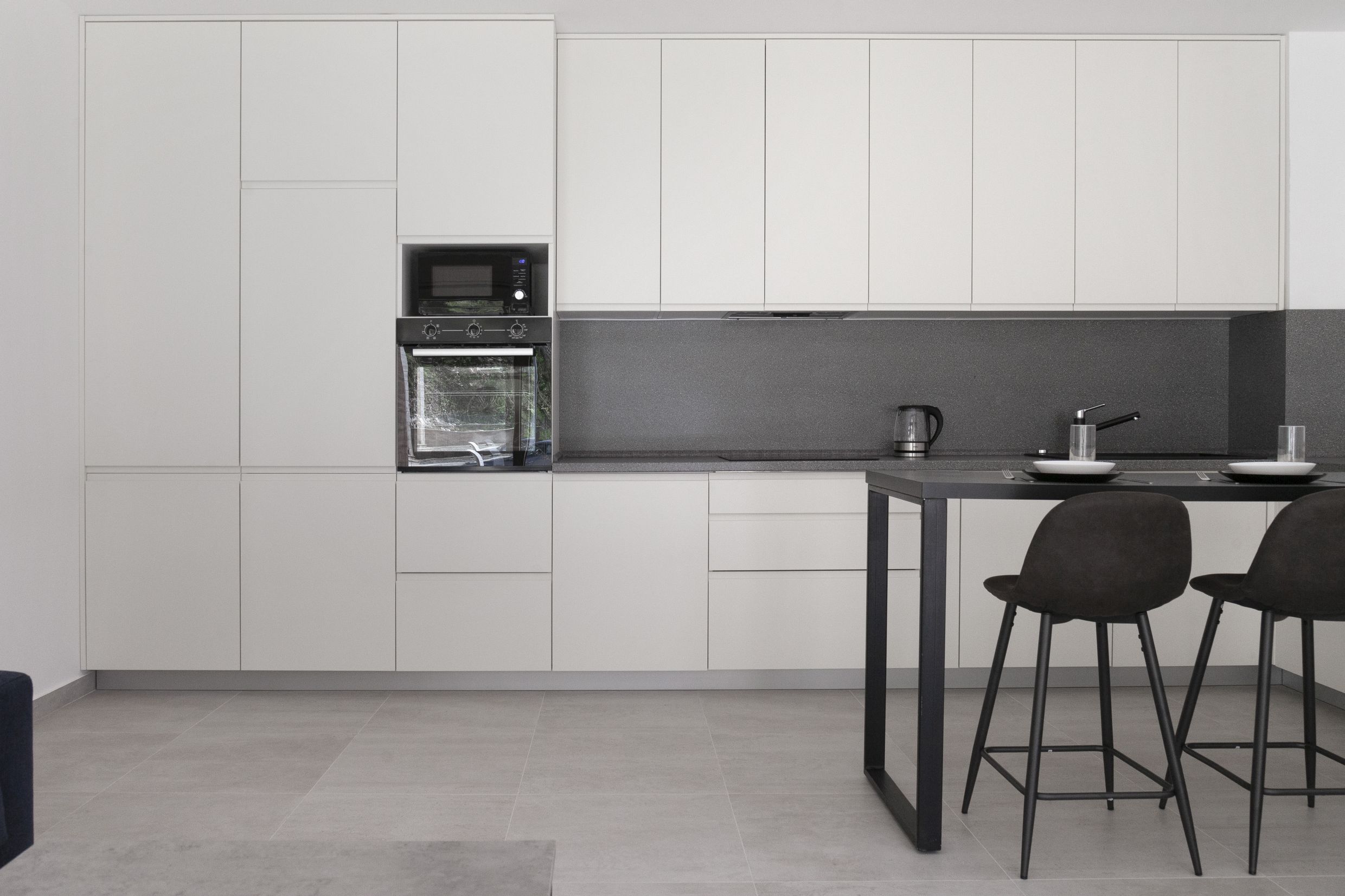 Moderne weiße Küche mit Bartheke in einer Wohnung in Kotor, Montenegro: Einbaugeräte und grauer Spritzschutz.
