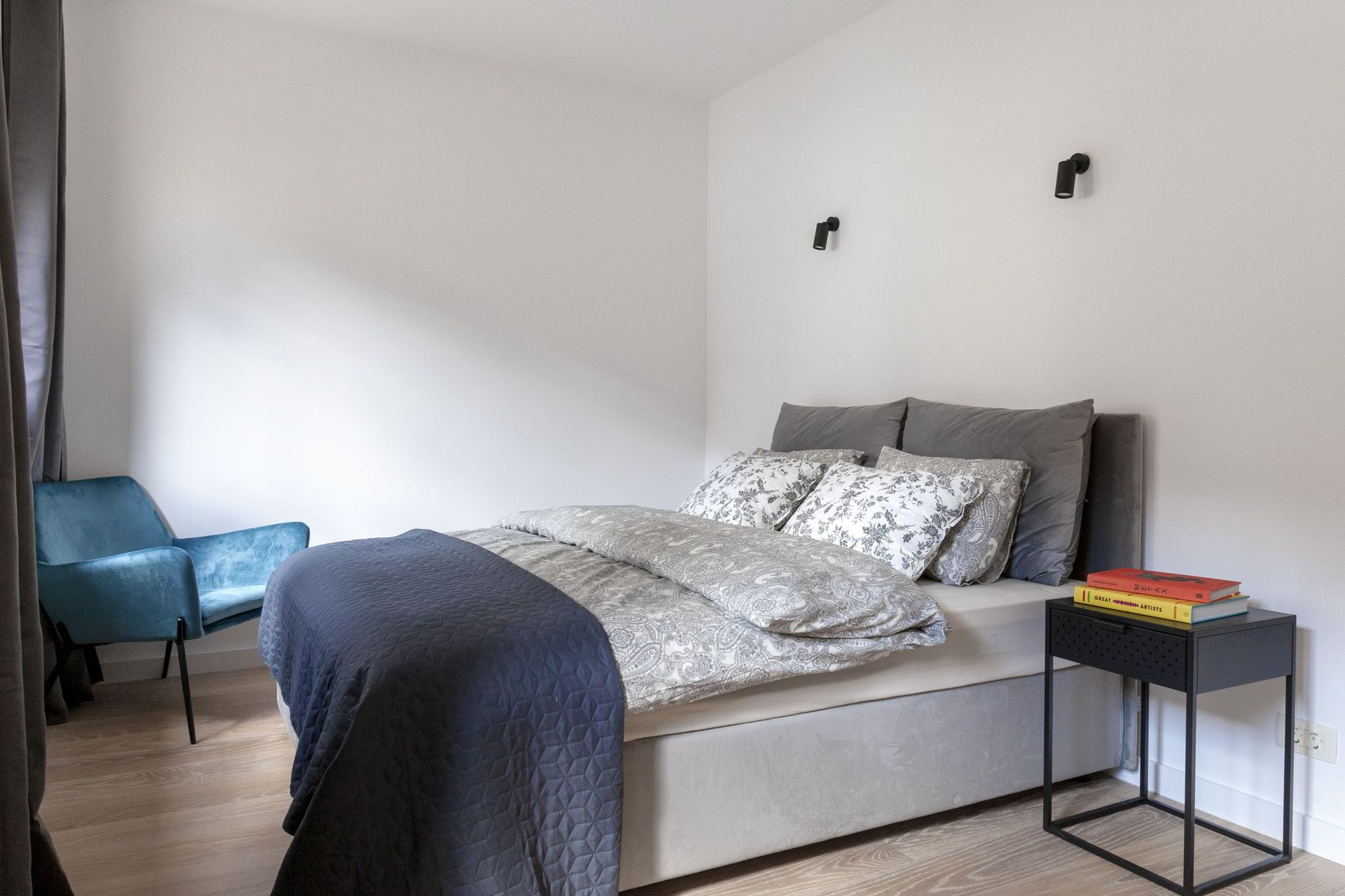 Modernes Schlafzimmer in einer Wohnung in Kotor, Montenegro: Doppelbett, blauer Sessel und stilvolle Wandleuchten.