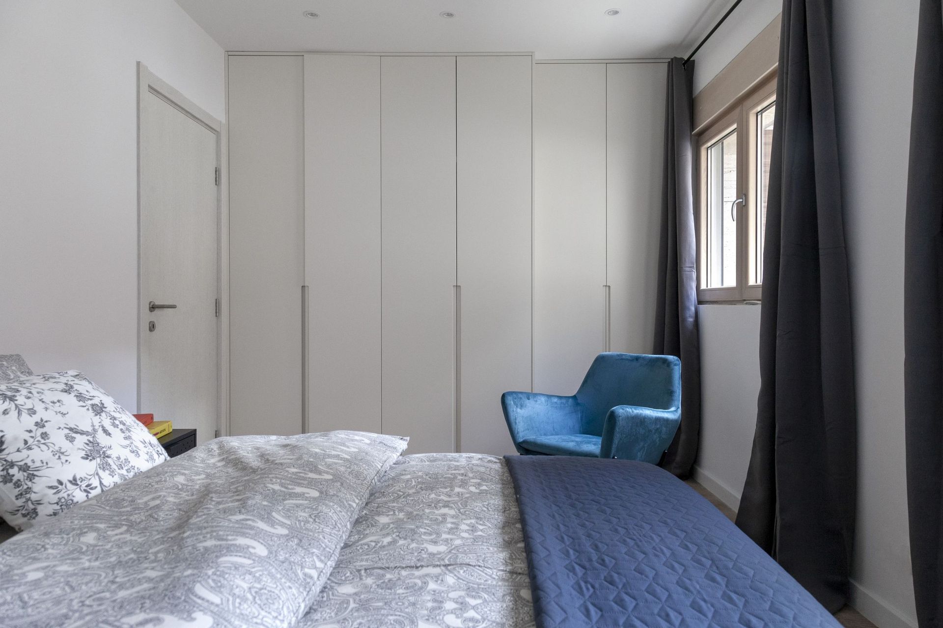 Modernes Schlafzimmer in einer Wohnung in Kotor, Montenegro: Einbauschrank, Bett mit Muster und blauer Sessel am Fenster.