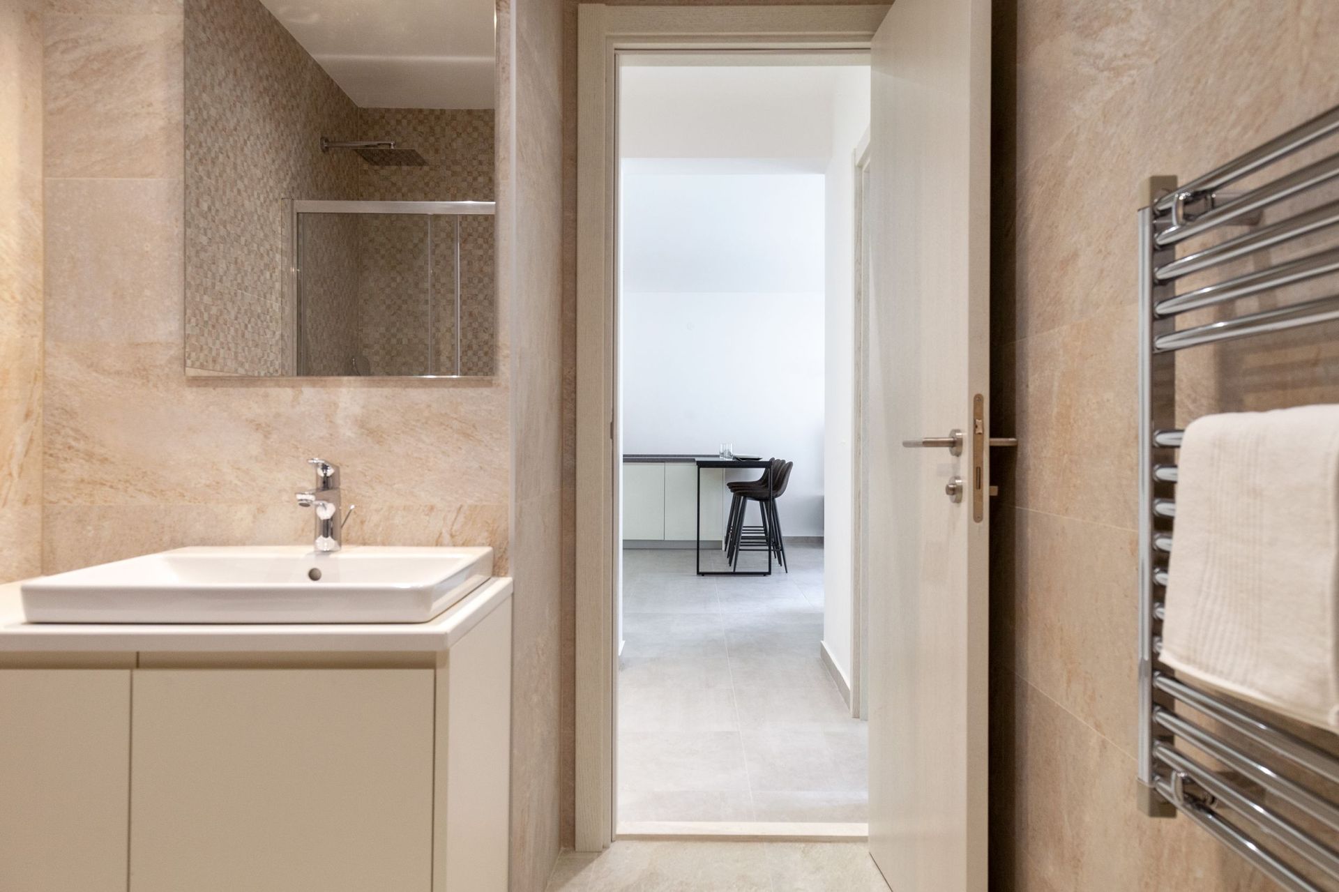 Modernes Badezimmer mit beigen Fliesen in einer Wohnung in Kotor, Montenegro, Blick auf die Küche mit Barhocker.