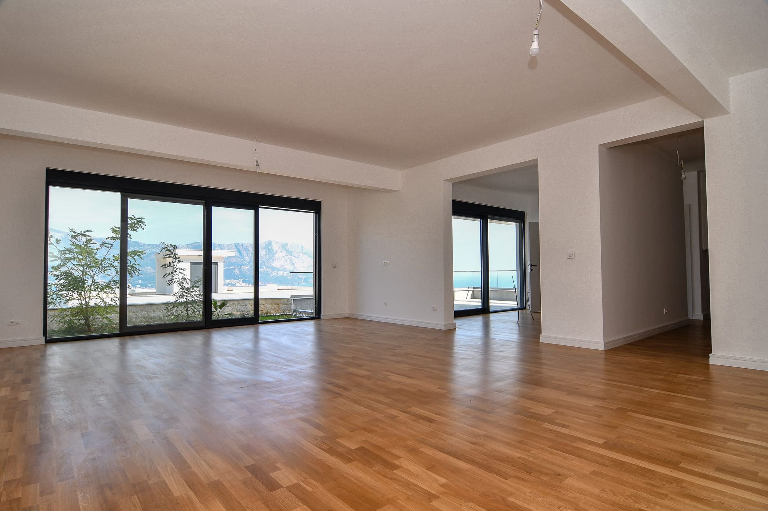 Geräumiges Wohnzimmer mit Panoramafenstern und Meerblick in einer neuen Villa in Budva, Montenegro, Parkettboden.