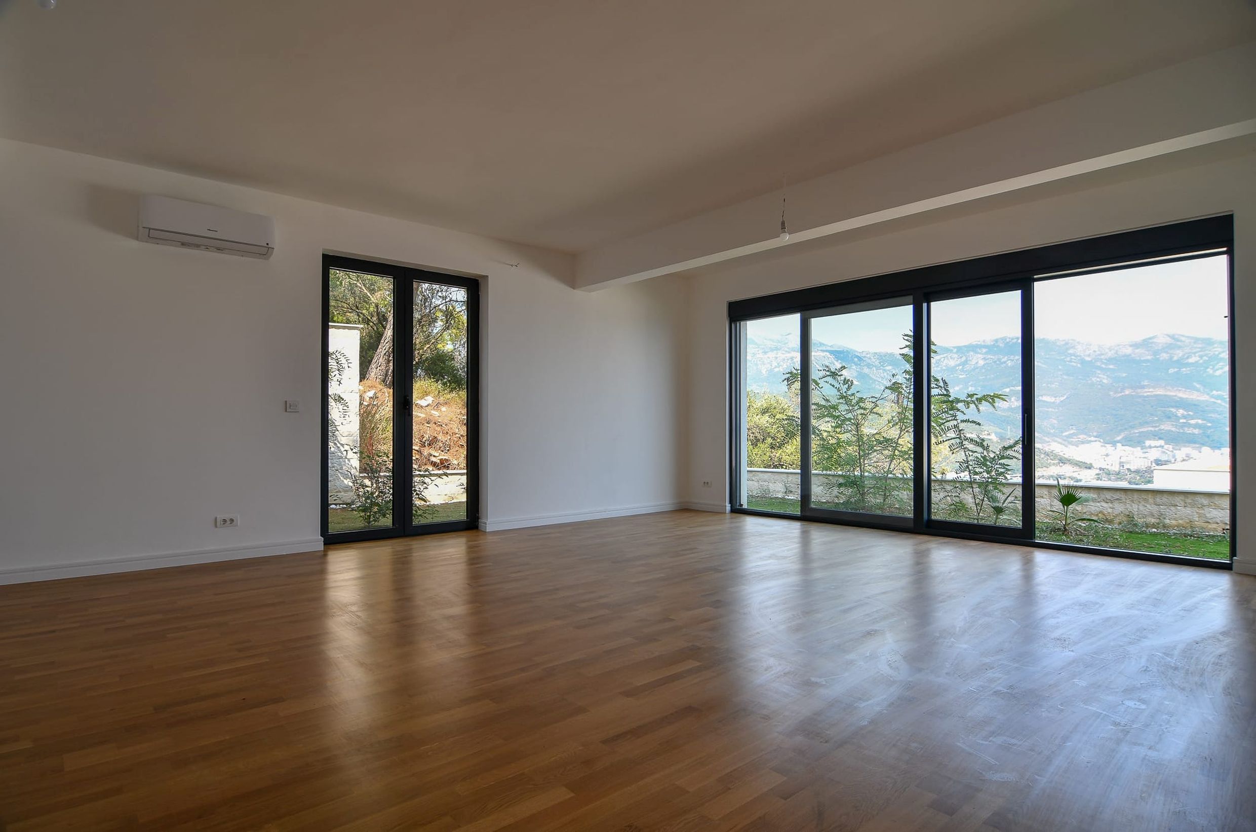 Helles Wohnzimmer mit Panoramafenstern und Bergblick in einer Villa in Budva, Montenegro: Parkett und moderne Ausstattung.