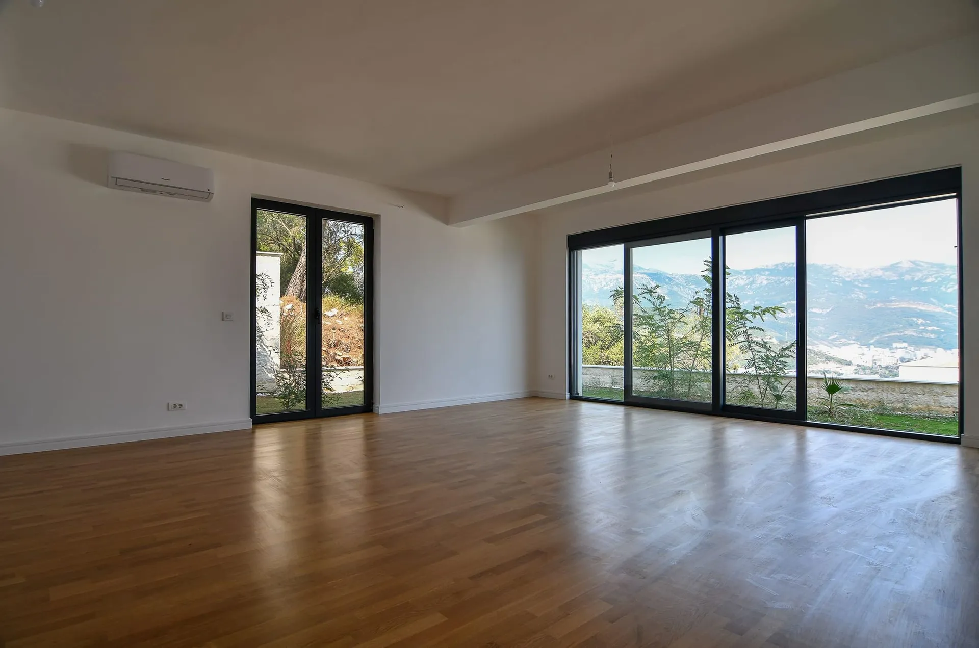Salon lumineux avec baies vitrées panoramiques et vue sur les montagnes dans une villa à Budva, Monténégro : parquet et finitions modernes.