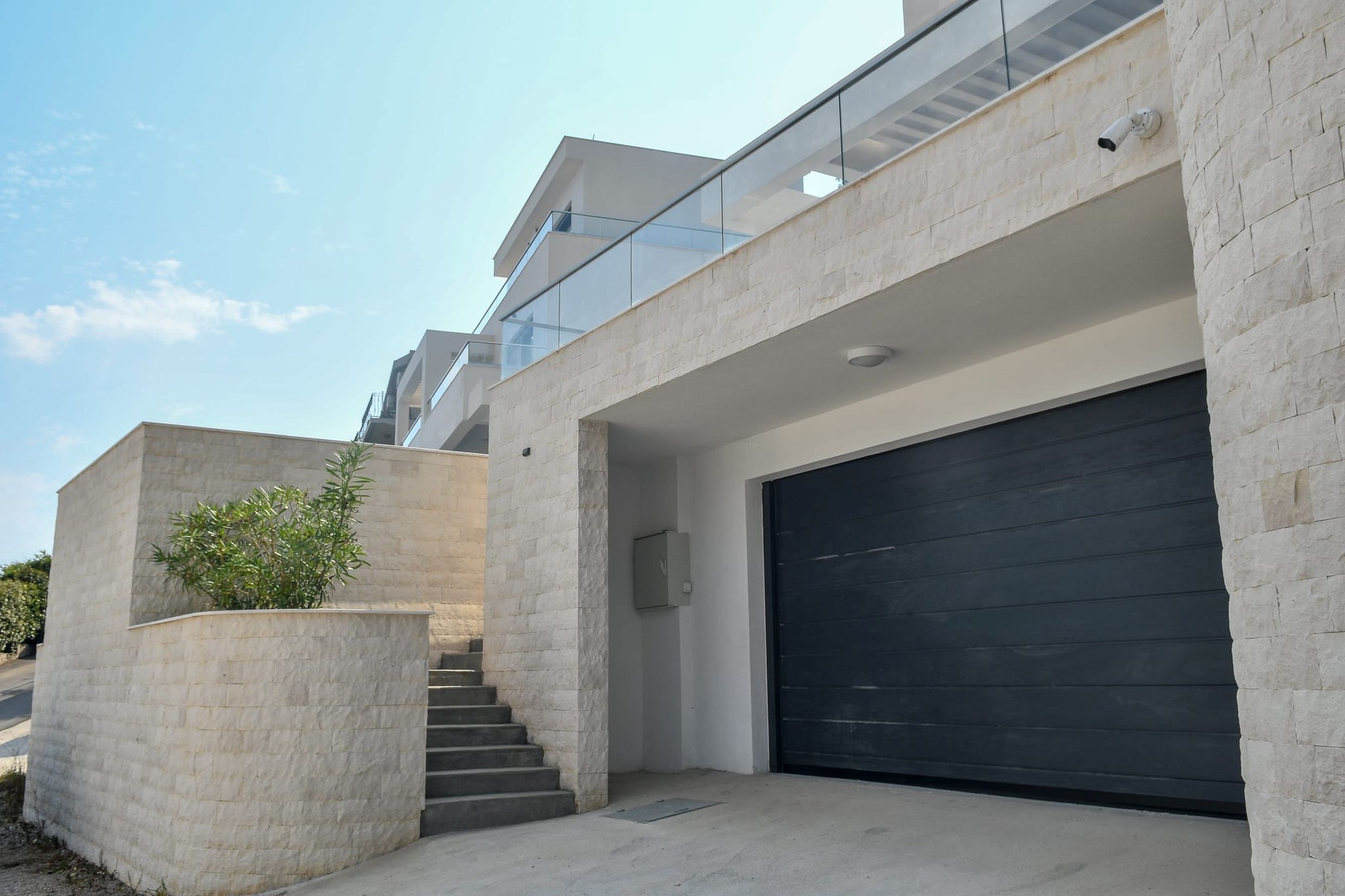 Moderne Villa in Budva, Montenegro: Fassade mit Steinverkleidung, Garagentor und Treppe zur Terrasse.