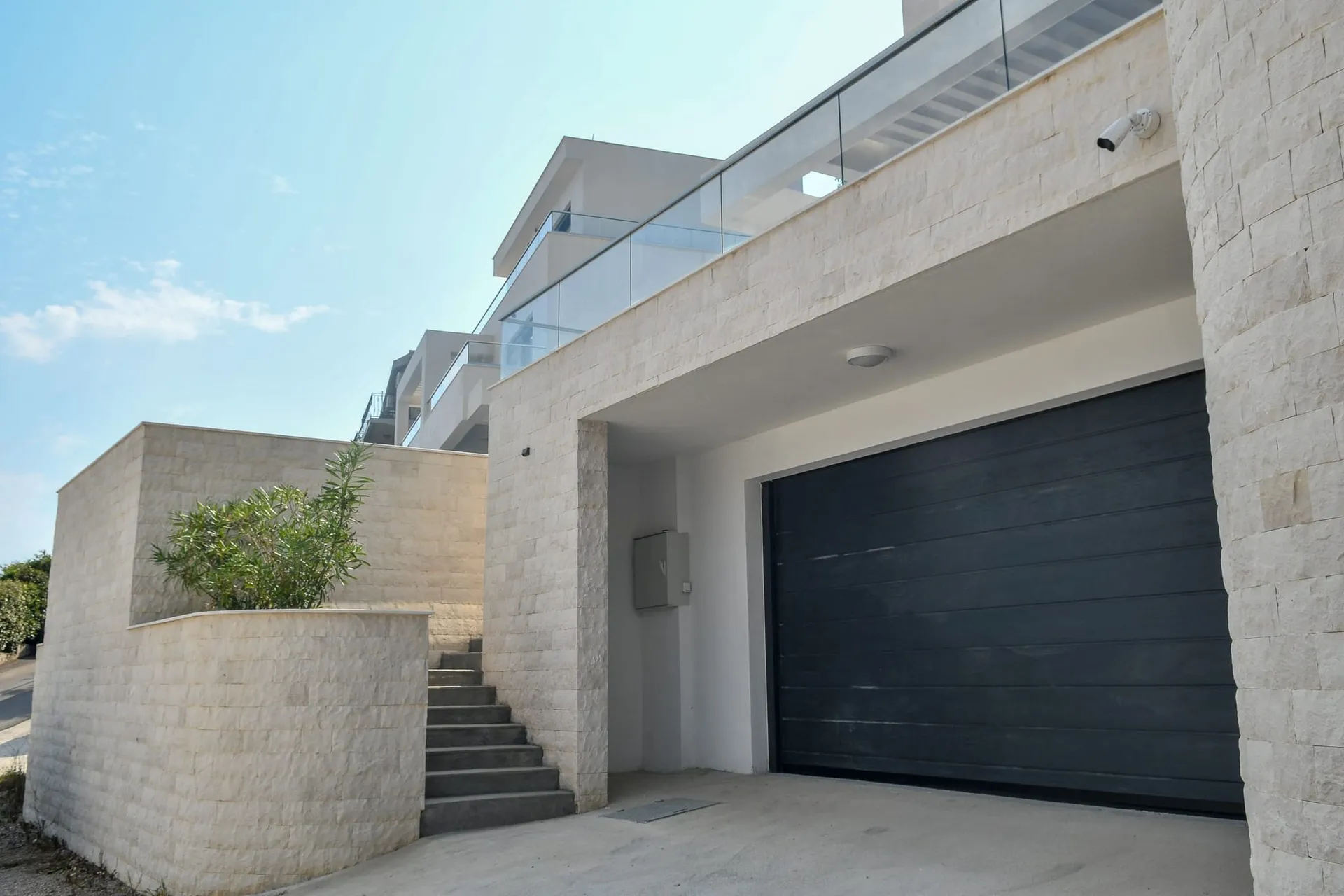 Villa moderne à Budva, Monténégro : façade avec parement en pierre, porte de garage et escalier menant à la terrasse.
