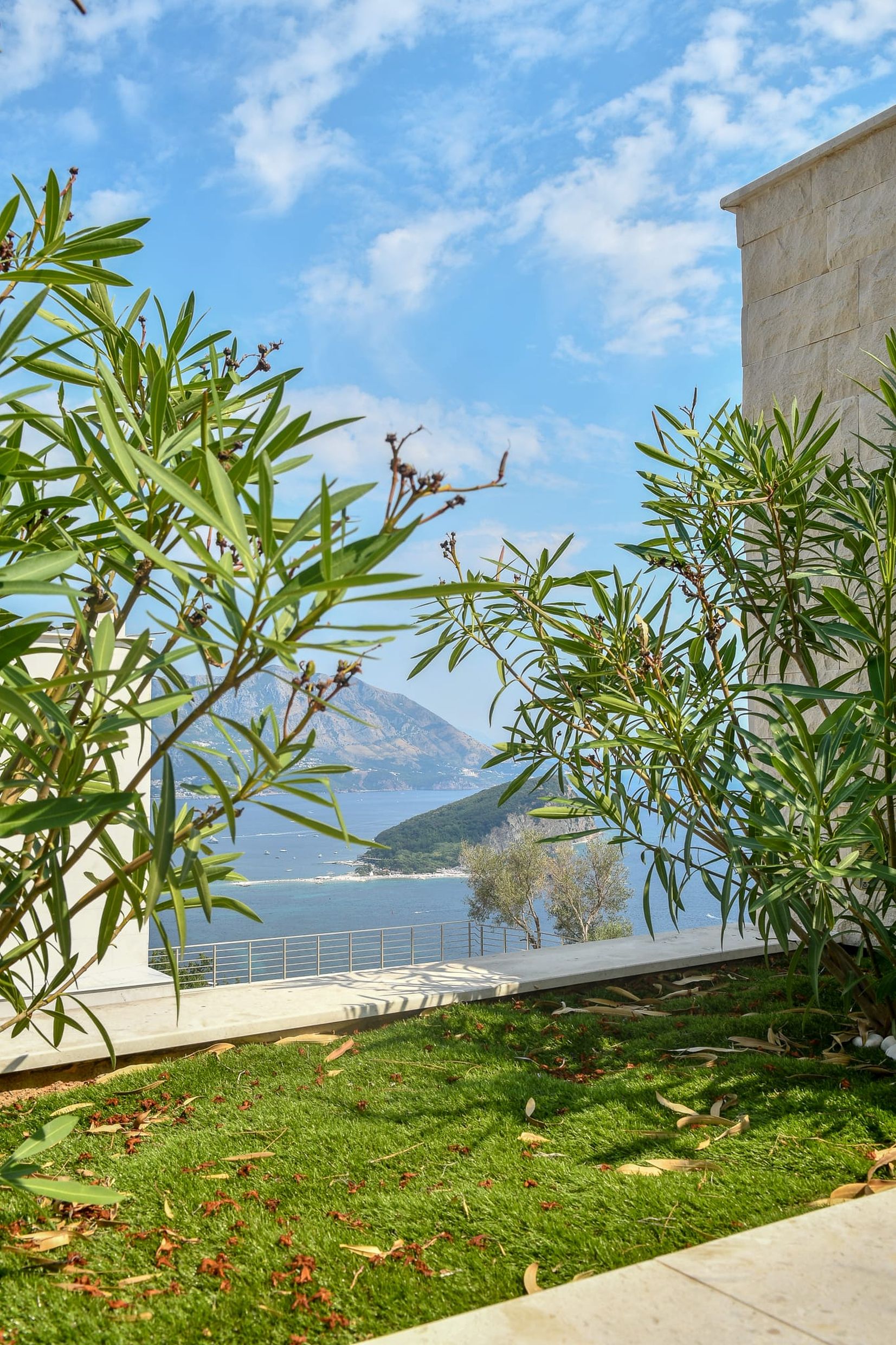 Blick von der Terrasse der Villa in Budva, Montenegro: Panorama auf das Meer, die Insel Sveti Nikola und die Berge durch das Grün des Gartens.