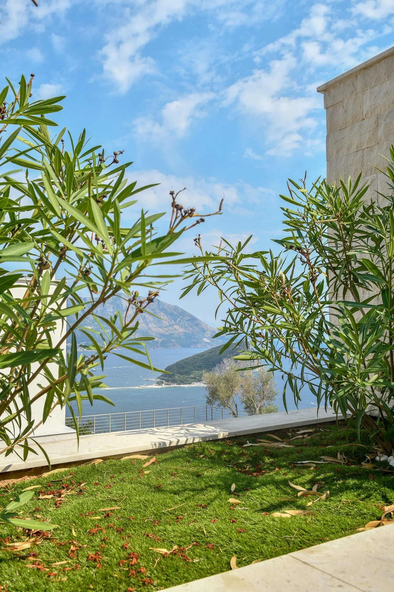 Vue depuis la terrasse d’une villa à Budva, Monténégro : panorama sur la mer, l’île Saint-Nicolas et les montagnes à travers la verdure du jardin.