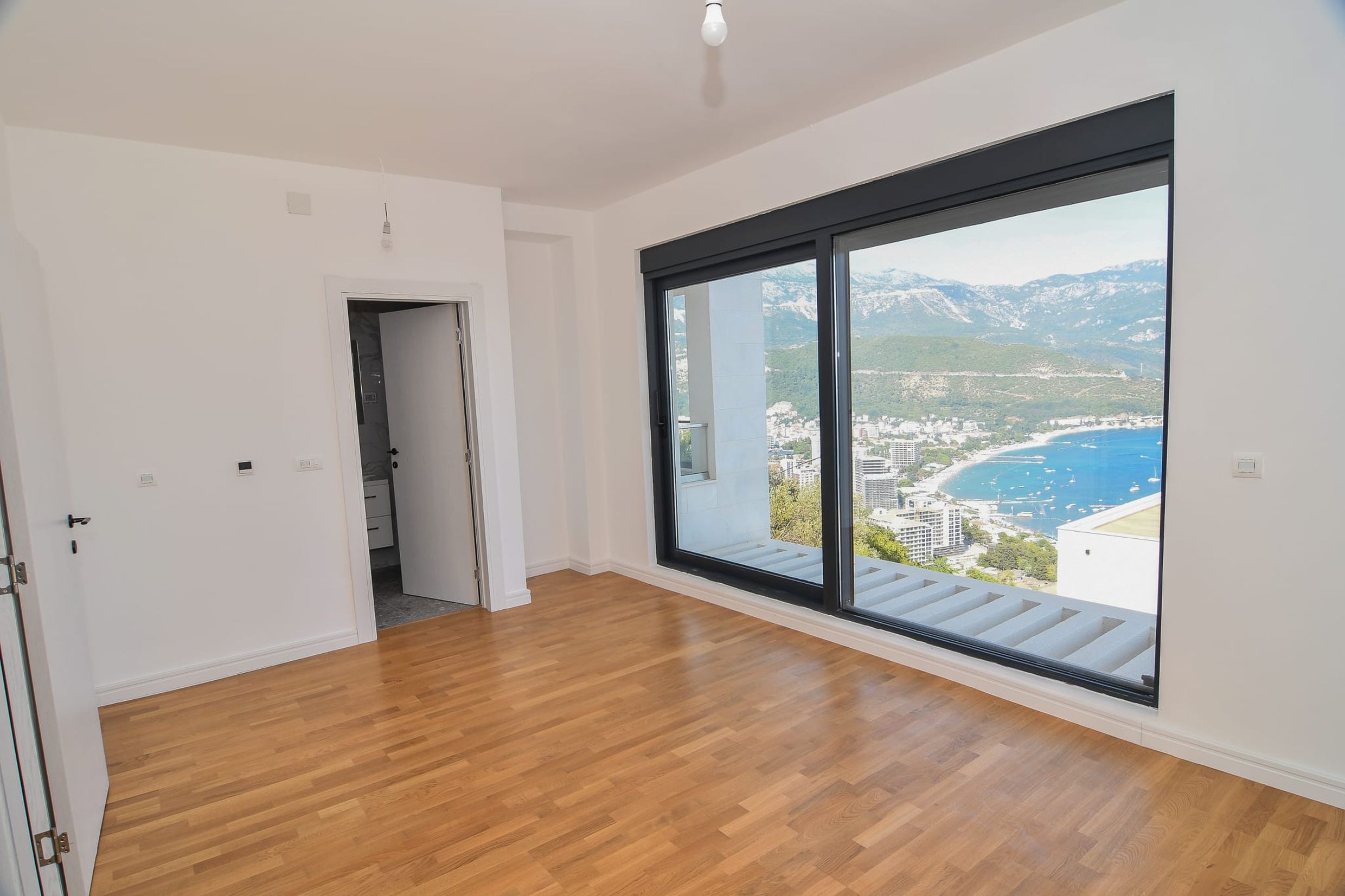 Helles Schlafzimmer in einer Villa in Budva, Montenegro, mit Panoramablick auf das Meer, die Berge und Parkettboden.