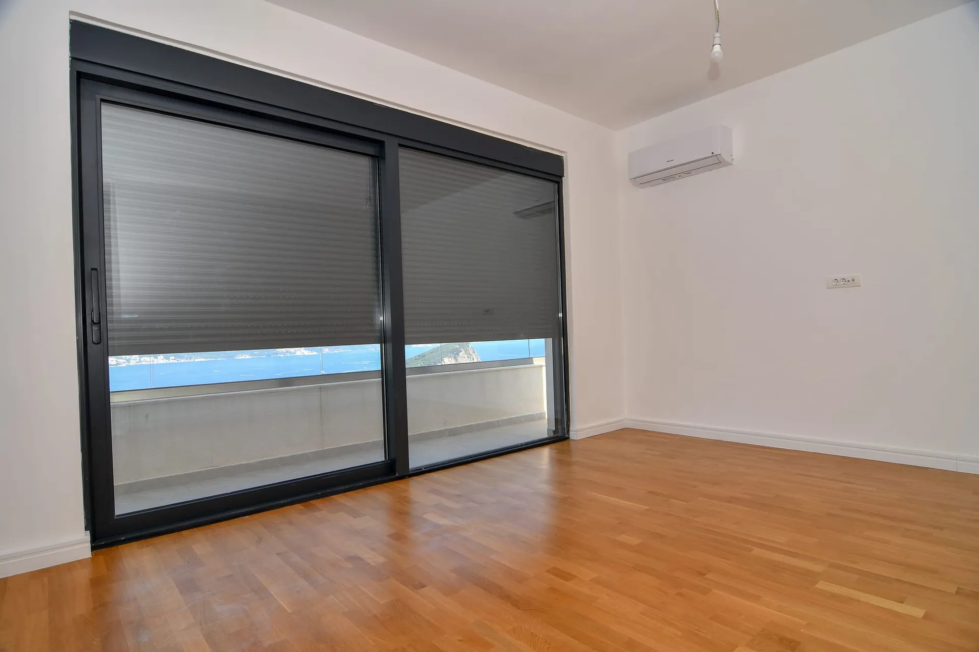 Salon lumineux avec baie vitrée panoramique, vue sur la mer et terrasse dans une villa à Budva, Monténégro. Parquet et climatisation.