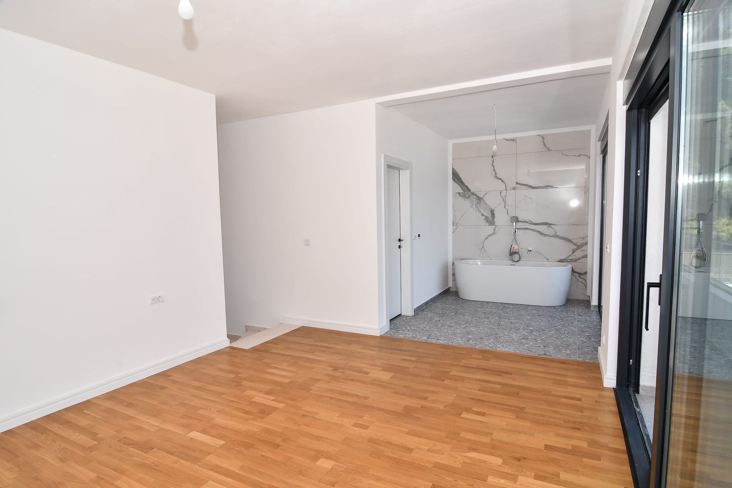 Schlafzimmer mit Bad in einer modernen Villa in Budva, Montenegro: Parkettboden, Panoramafenster und Marmorverkleidung.