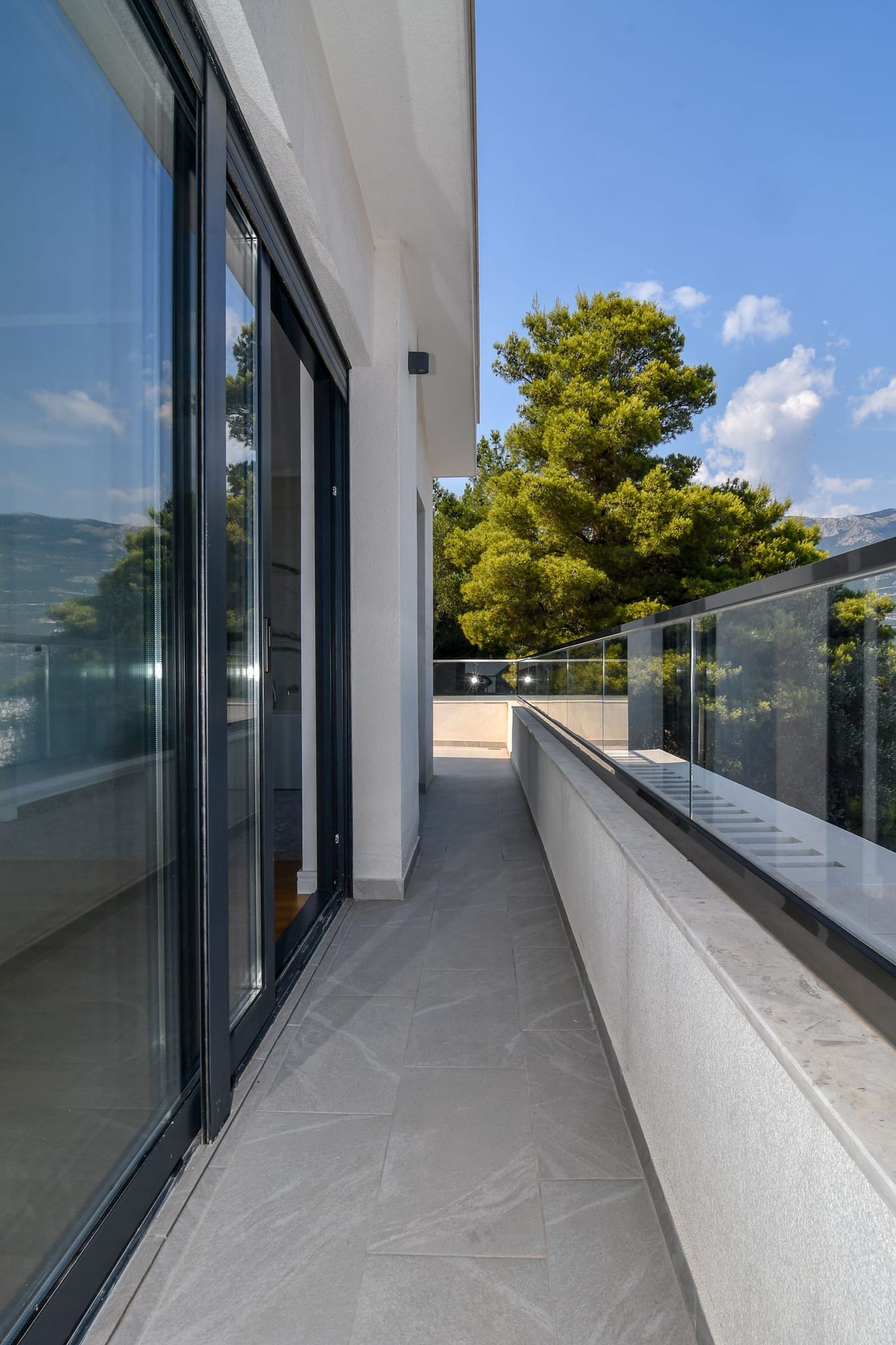 Geräumiger Balkon der Villa in Budva, Montenegro, mit Panoramaverglasung, Glasgeländer und Blick ins Grüne.