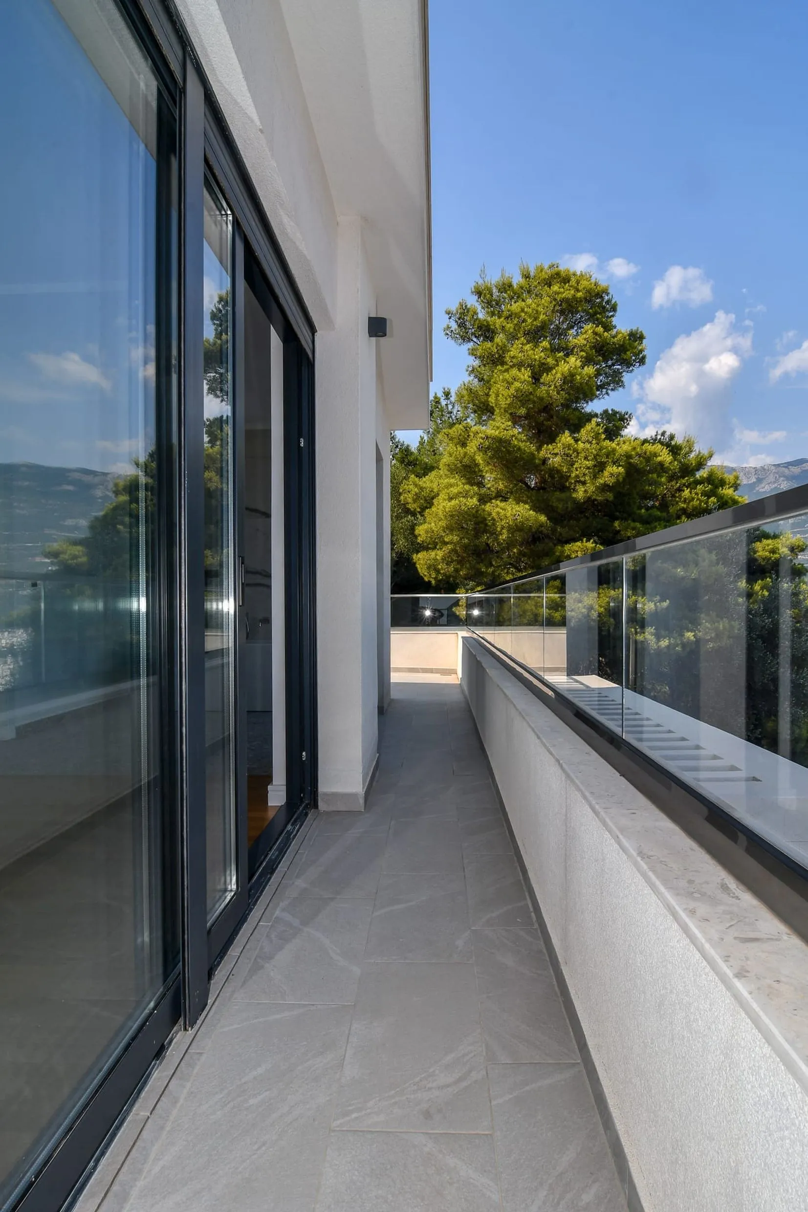 Spacieux balcon de la villa à Budva, Monténégro, avec baies vitrées panoramiques, garde-corps en verre et vue sur la verdure.