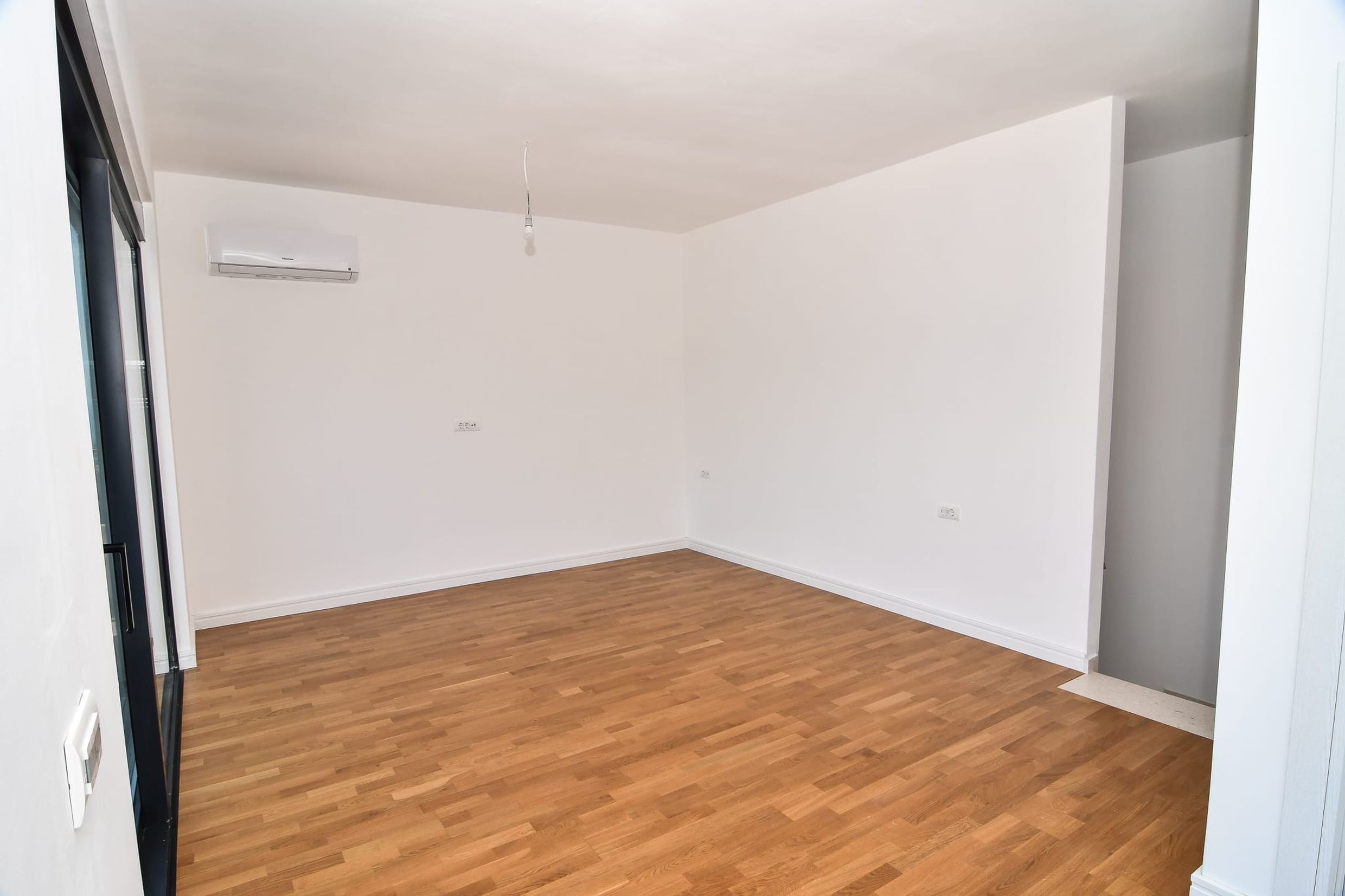 Helles Wohnzimmer mit Parkett und Klimaanlage in einer neuen Villa in Budva, Montenegro. Leerer Raum mit weißer Ausstattung.